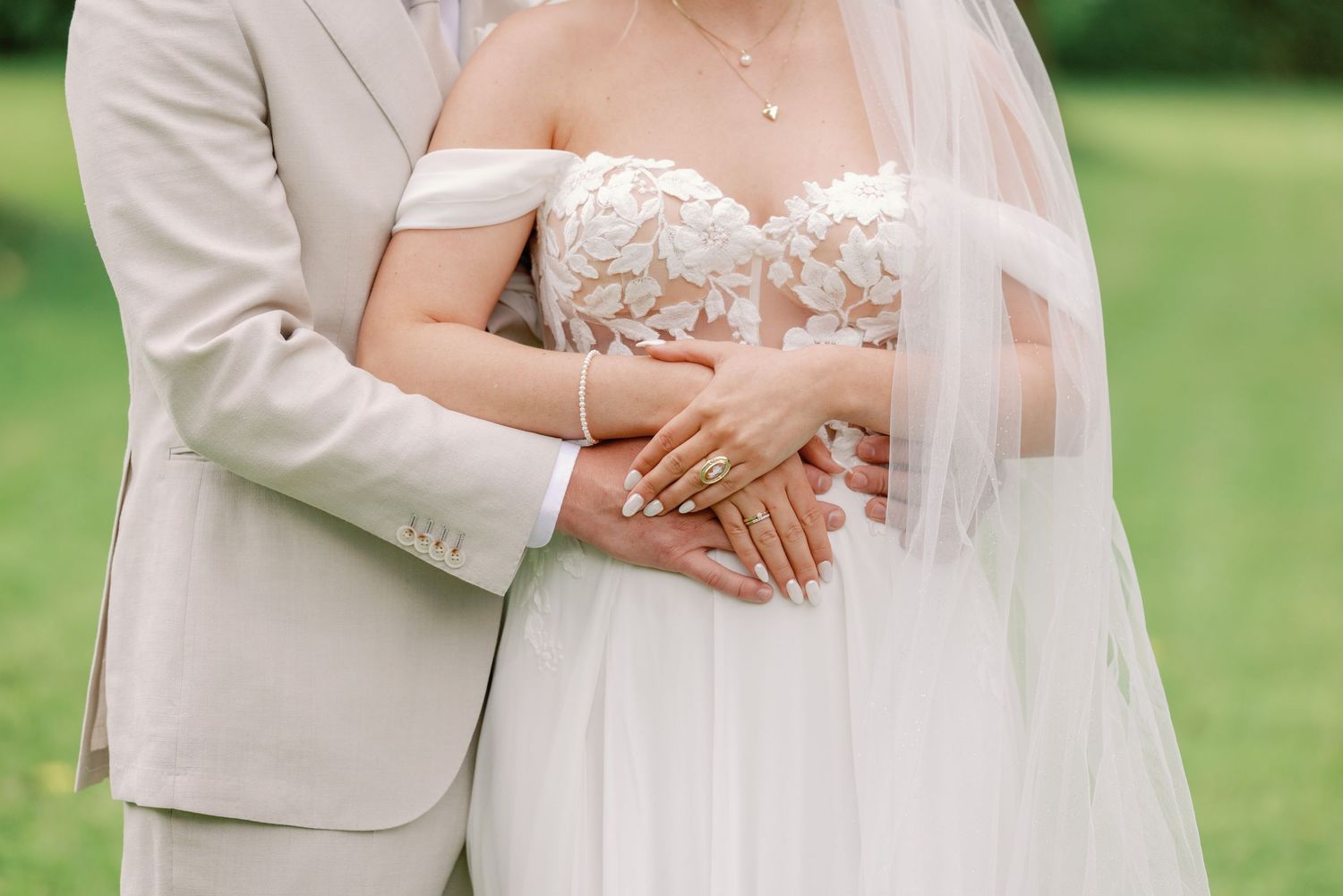A couple in wedding attire shares an intimate moment outdoors on a grassy lawn in soft natural lighting.