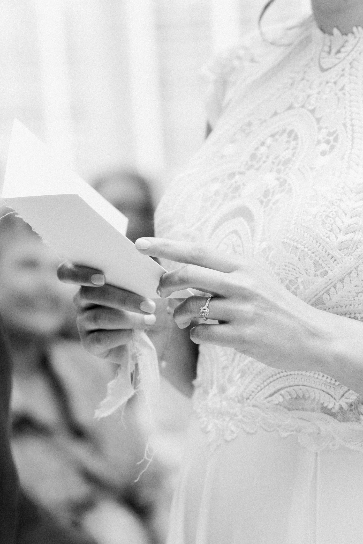Close-up black and white photo of hands holding a book or paper in elegant lace dress details.