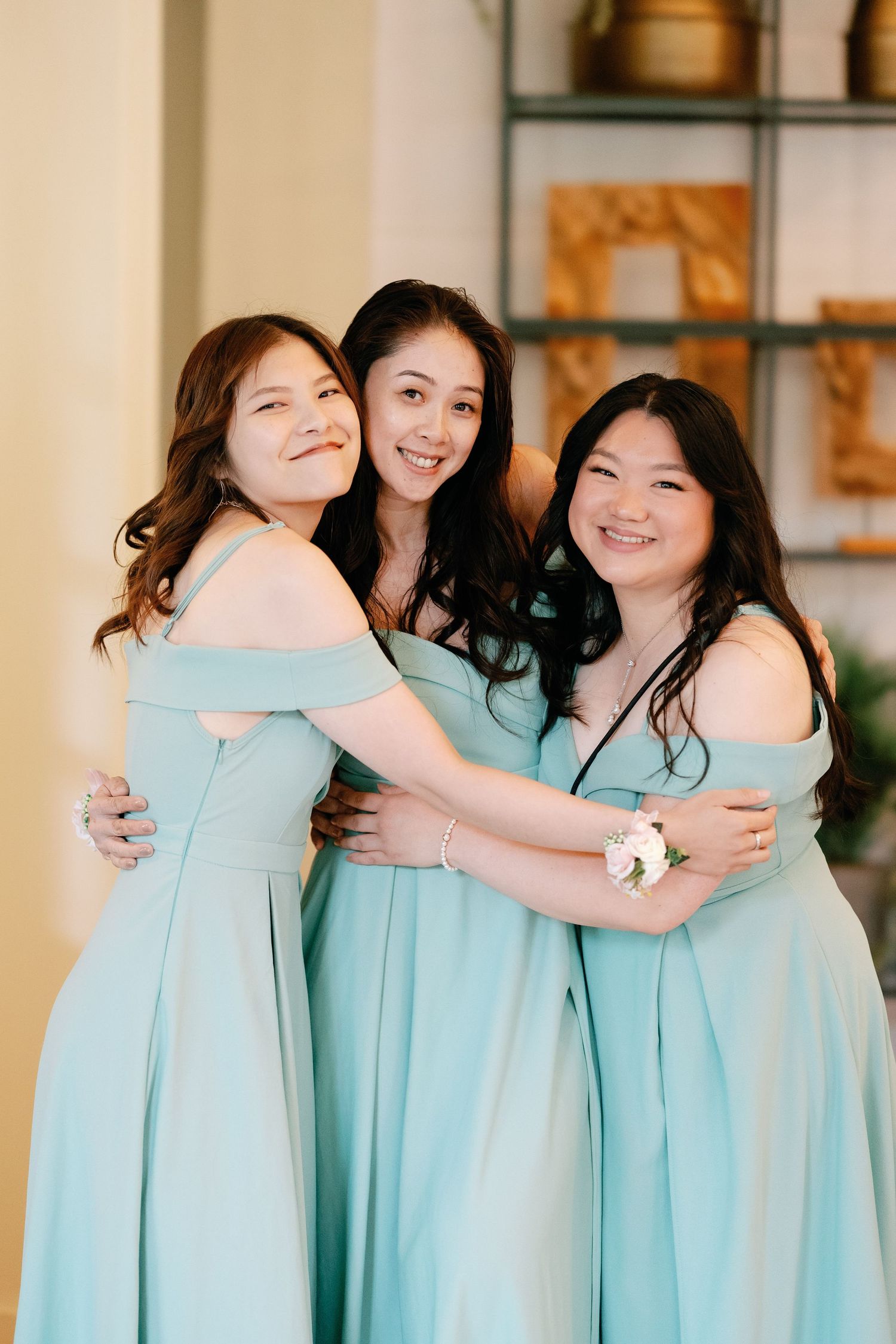 Three bridesmaids in matching mint green dresses share emotional hugs and smiles during a wedding celebration.