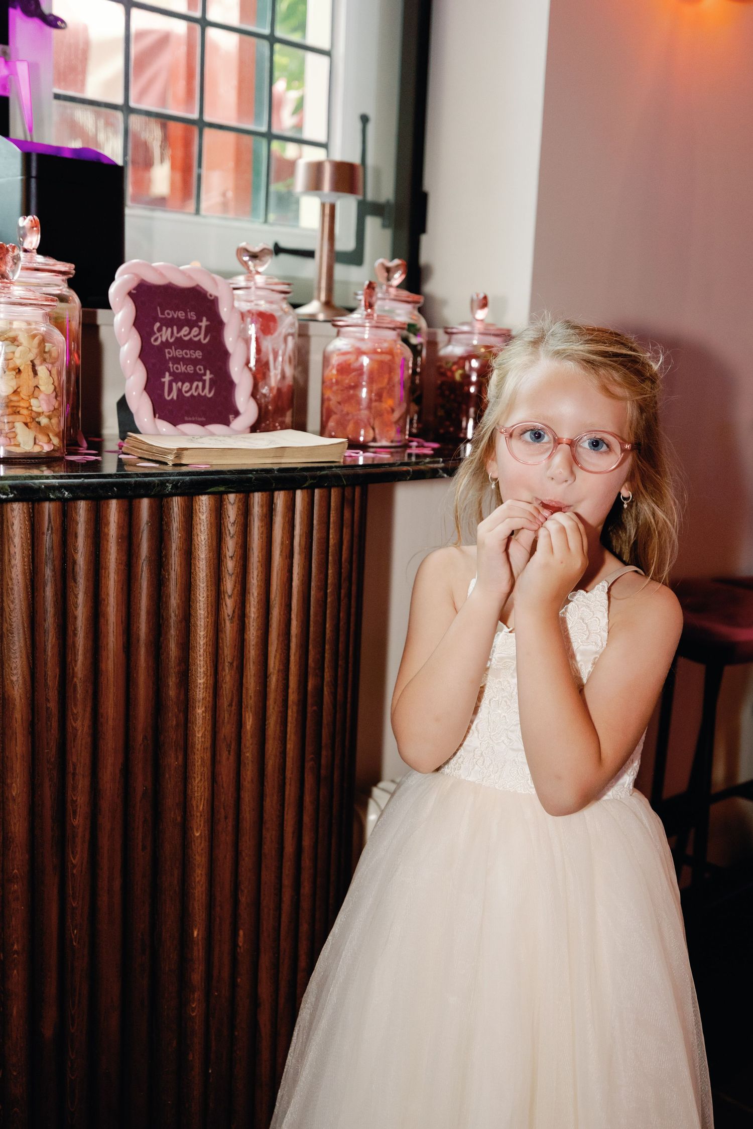 A young child in a white dress and glasses makes playful expressions in a series of four connected photos.