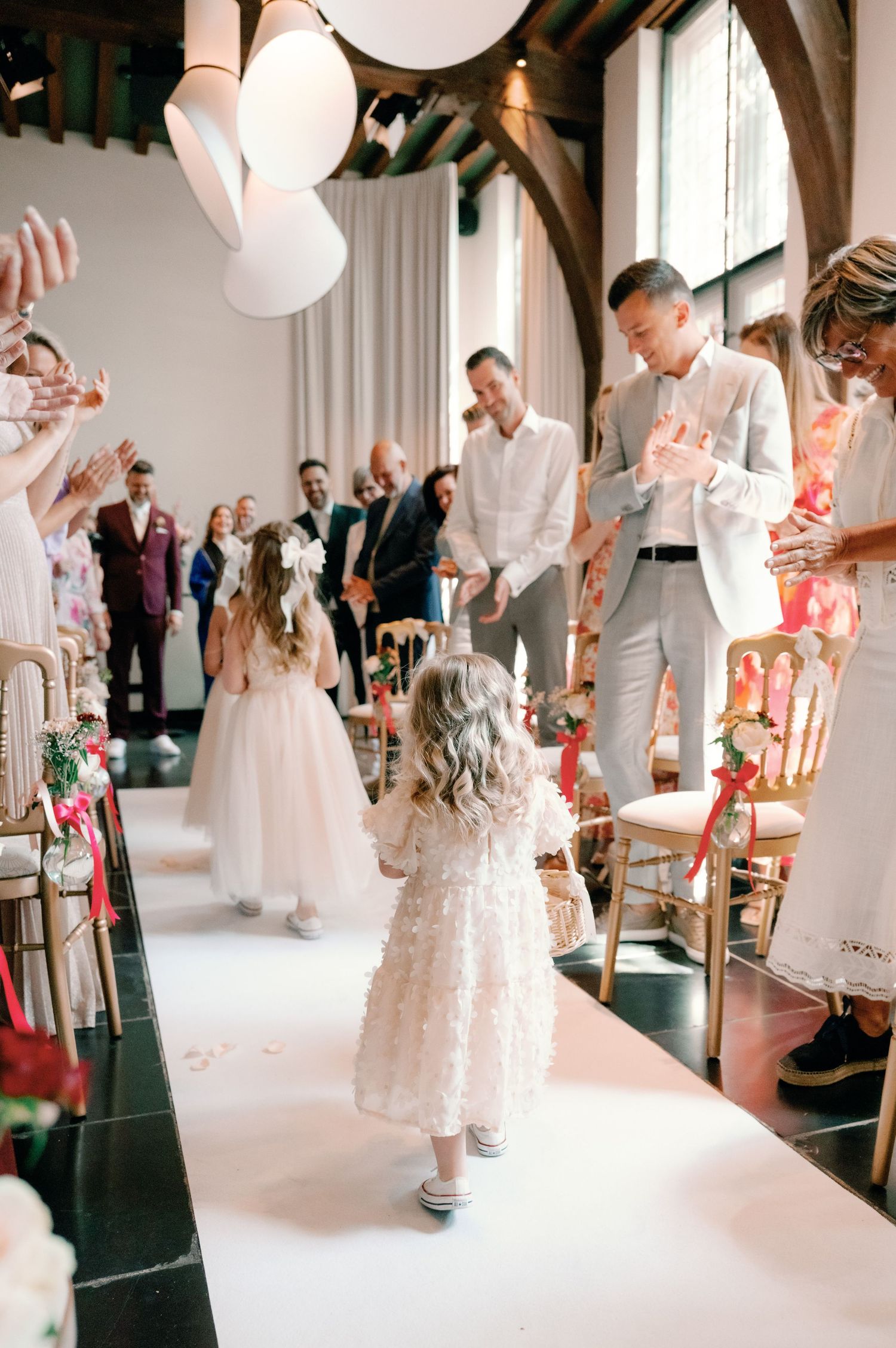 Wedding guests in white attire dance and celebrate at a bright indoor reception venue with paper lantern decorations.
