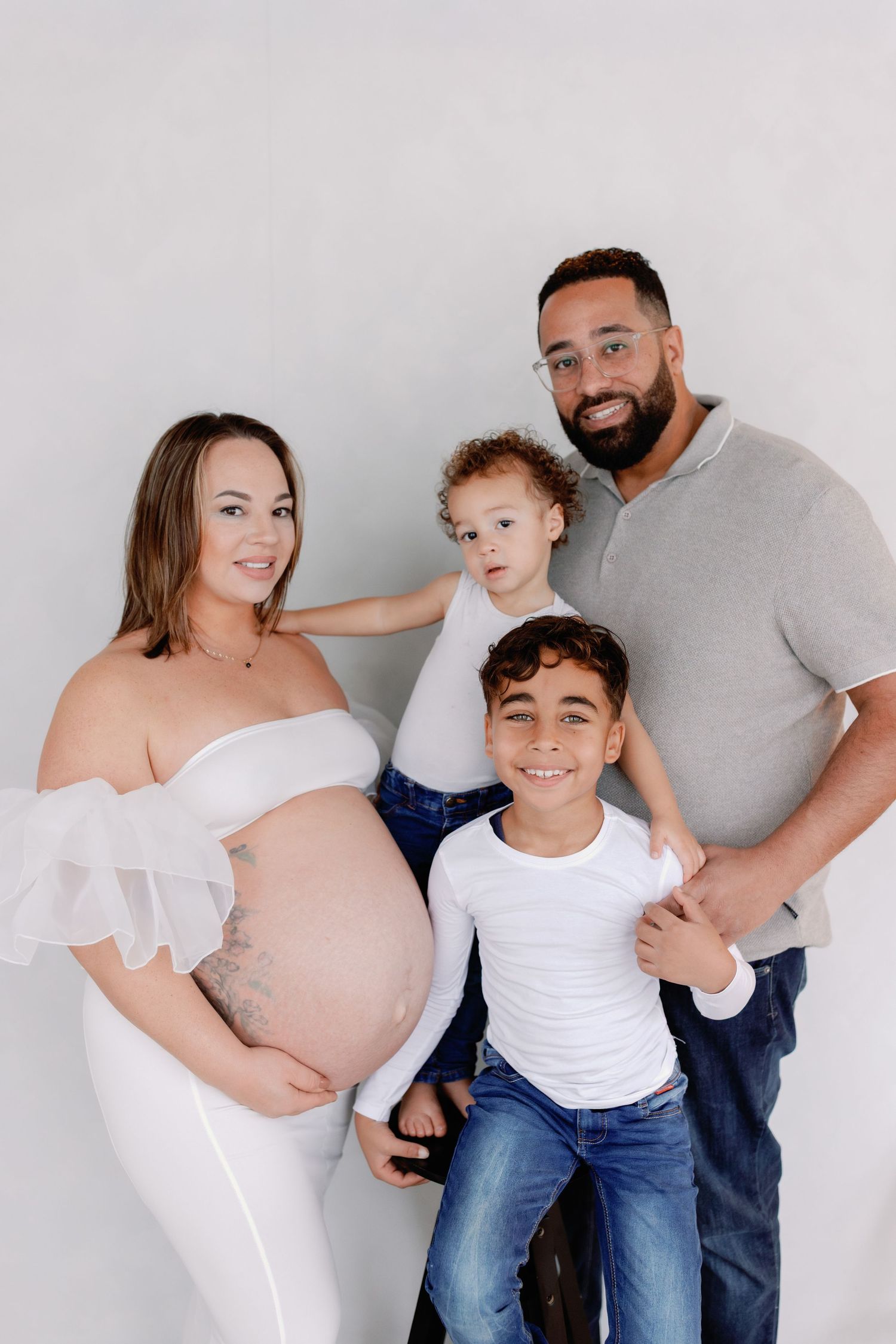 A maternity photo sequence showing a growing family posing together against a white background in coordinated outfits.