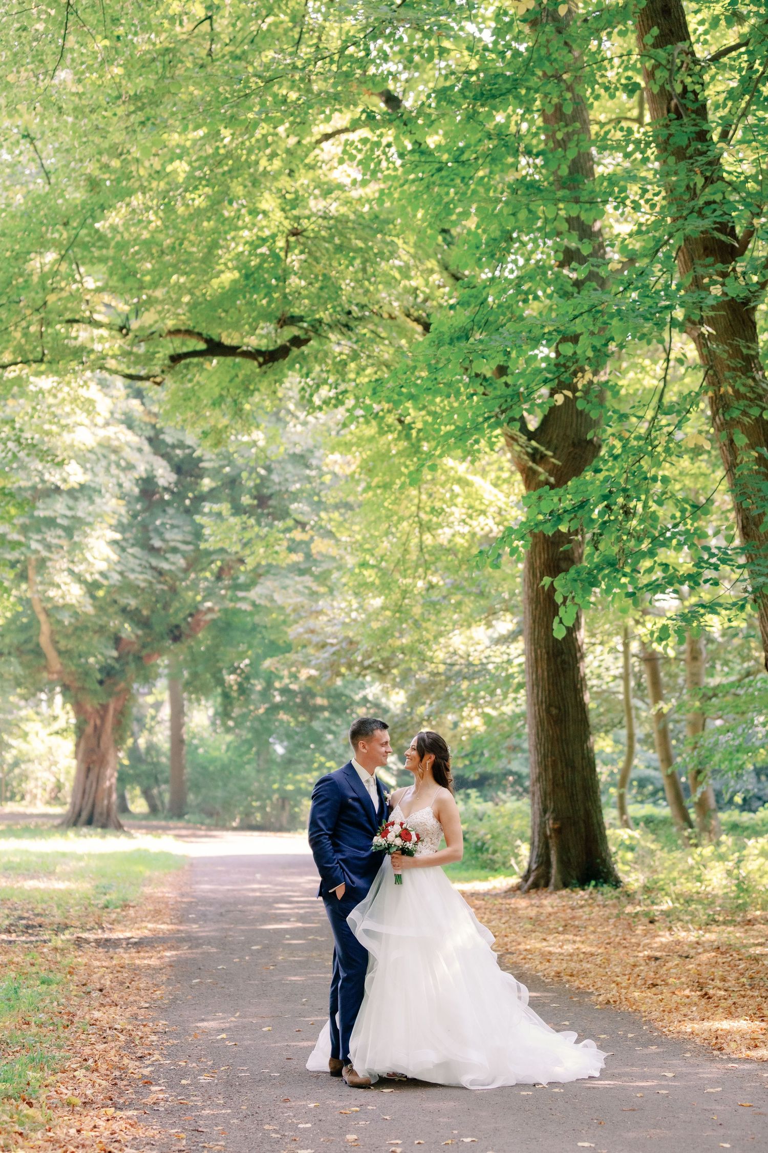 A wedding couple shares an intimate moment on a sunlit forest path surrounded by lush greenery.