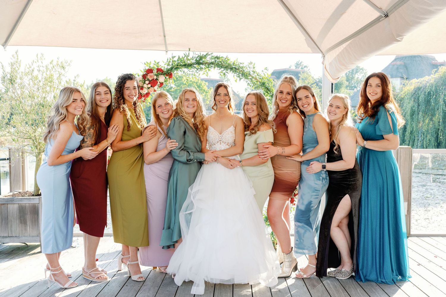 Bridesmaids in various shades of blue dresses pose together on outdoor deck.