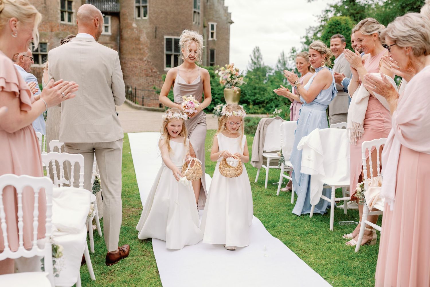 A wedding party in pink and white dresses reacts with joy and laughter during an outdoor celebration.