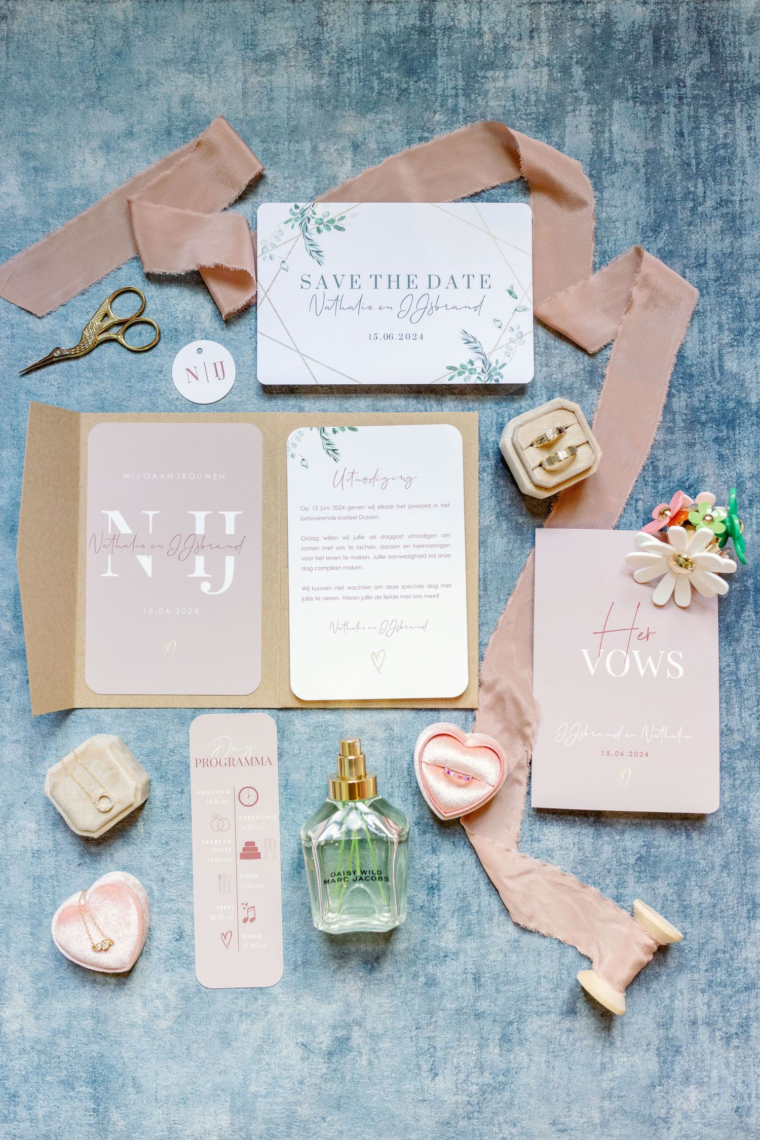 Elegant wedding stationery flatlay with blush ribbons, floral elements and vow cards on a textured blue background.