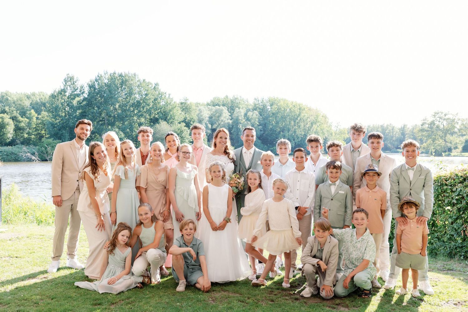 Wedding party in neutral beige and white attire poses together outdoors in a garden setting during summer celebration.