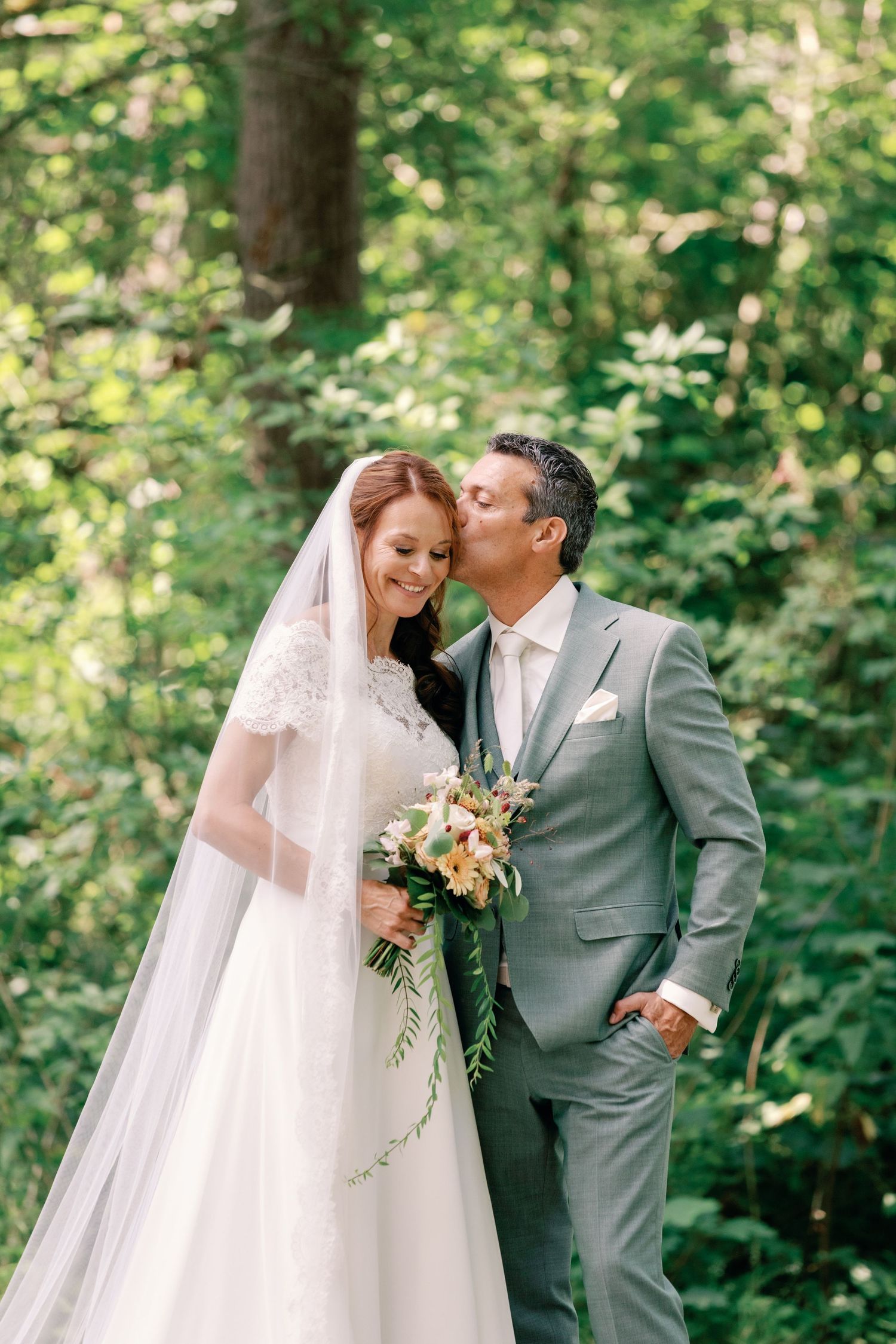 A bride and groom share romantic moments in a lush green forest setting during their outdoor wedding photoshoot.