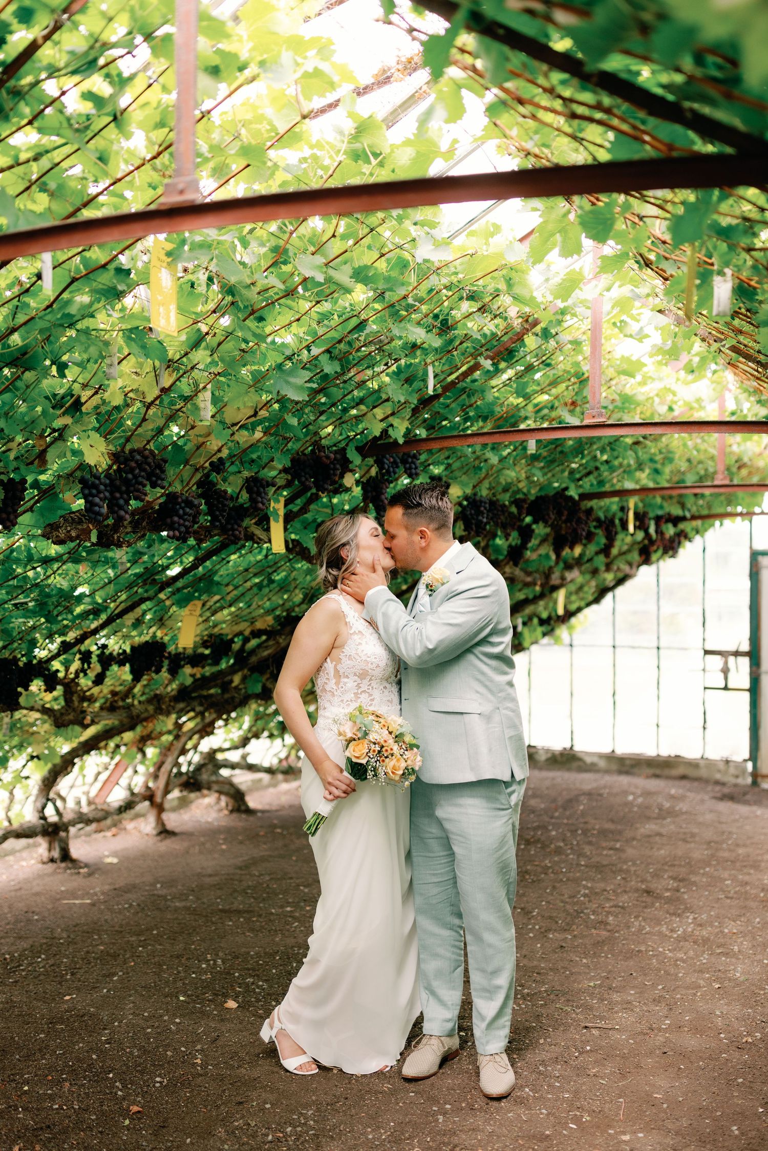 A couple shares an intimate moment under a lush green vine-covered arbor in a garden setting.