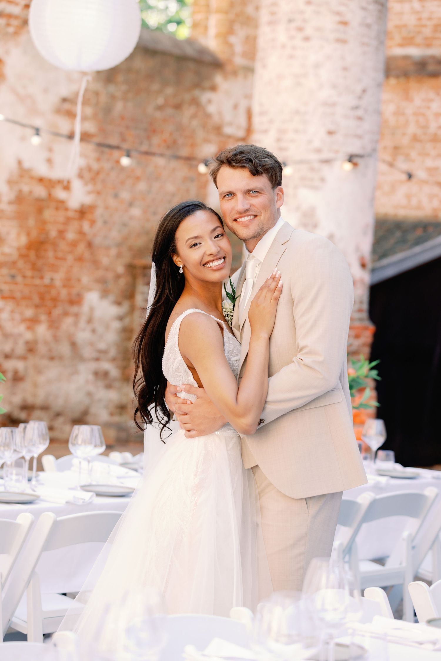 A happy couple embraces and laughs together at an elegant wedding reception venue with exposed brick walls and white decor.