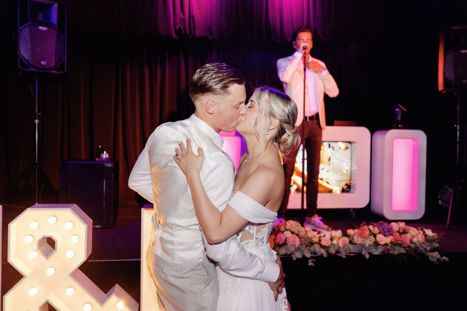Couples dancing together at a dimly lit wedding reception with purple and pink lighting effects.