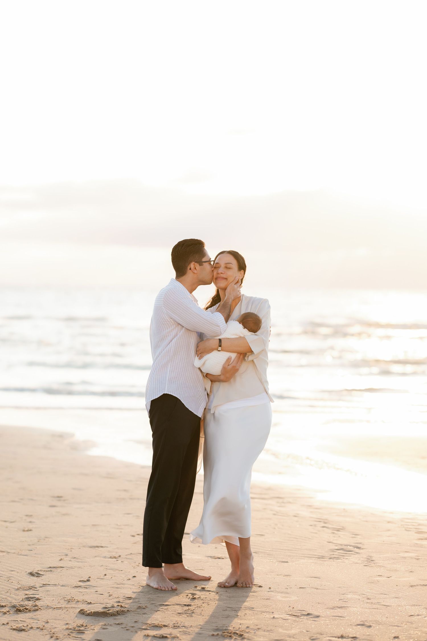 Family shares intimate moment together on sandy beach at sunset.