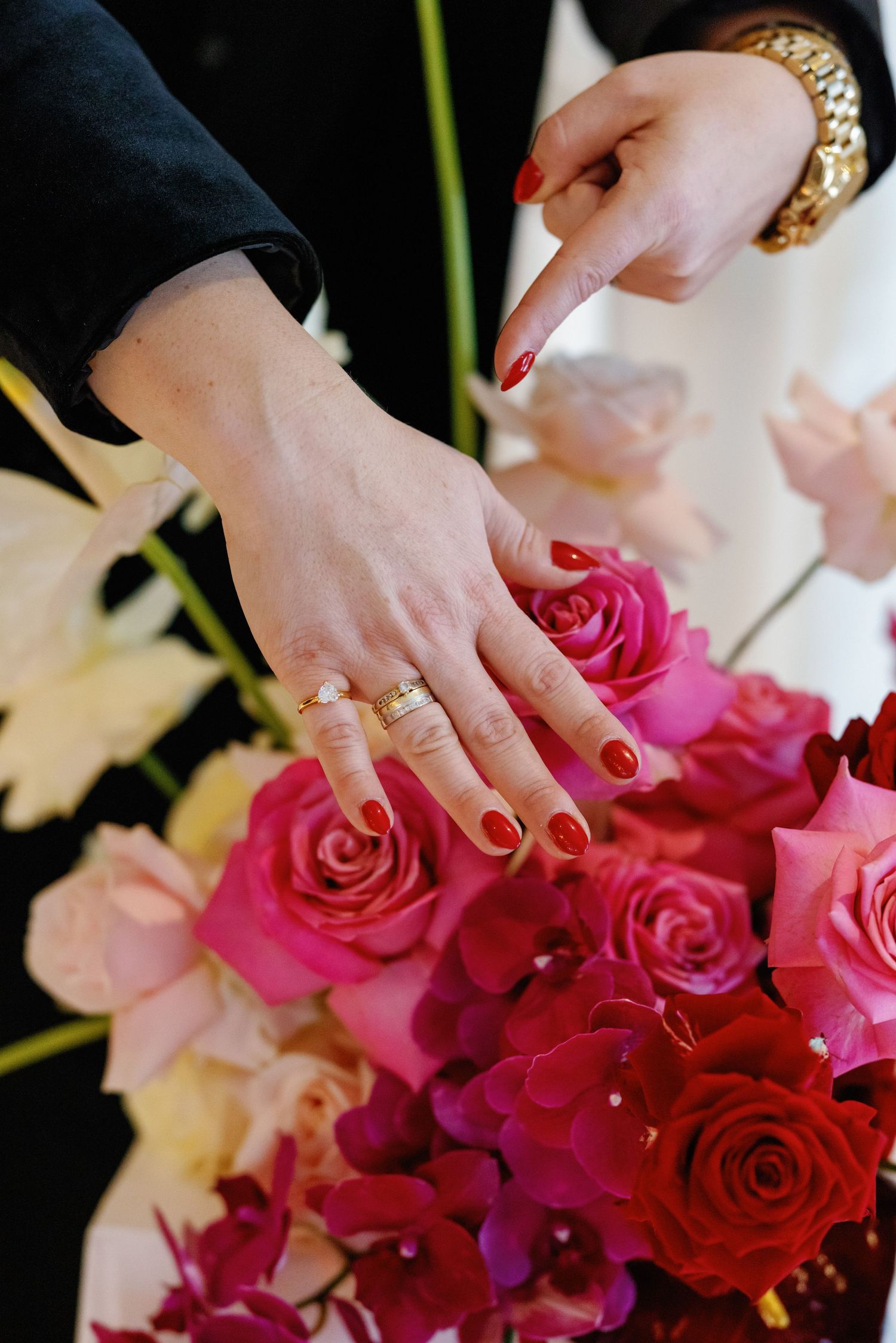 Hands arranging vibrant pink and red roses in an elegant floral arrangement with delicate petals.