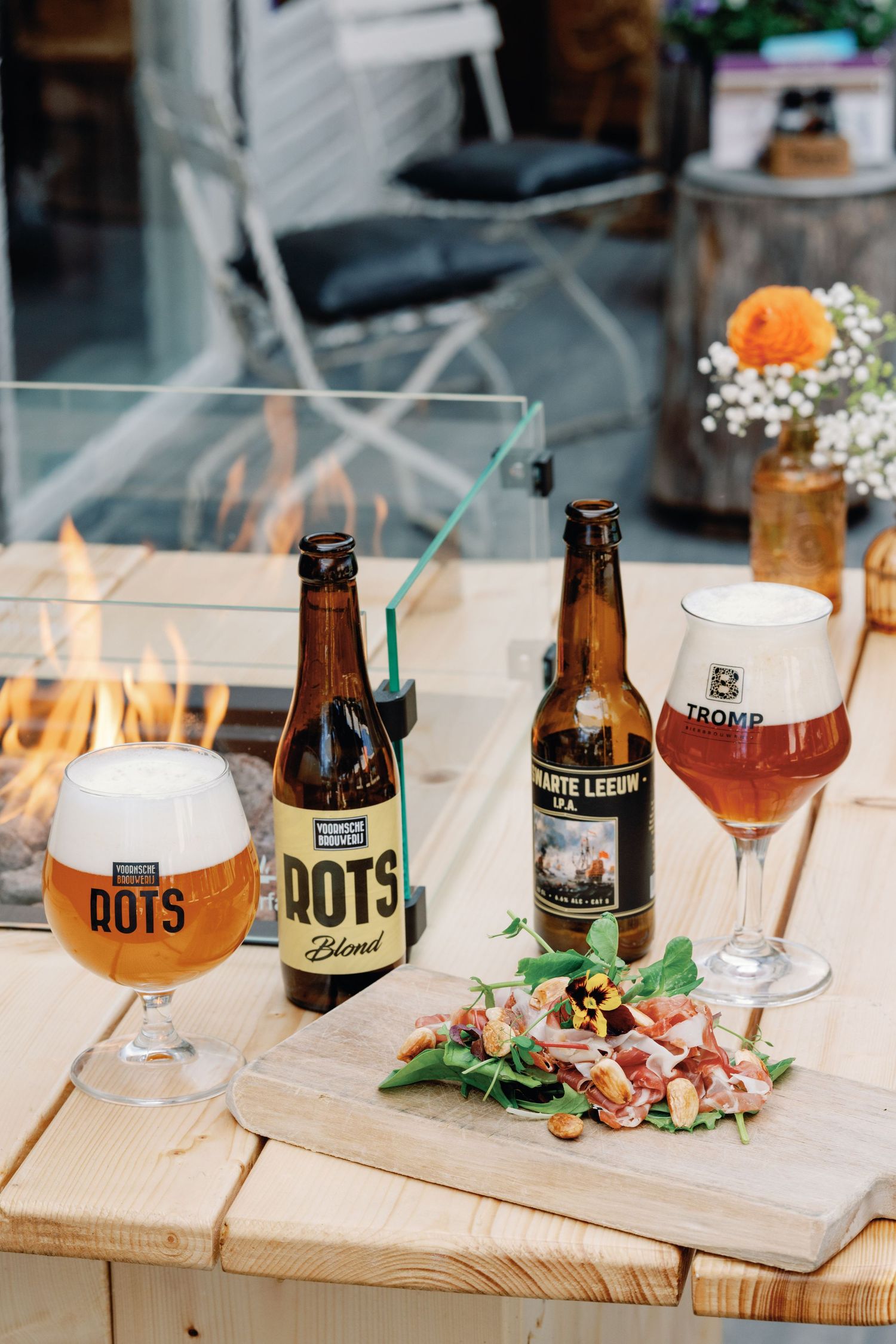 Wooden serving board displays craft beer bottles and cocktails alongside appetizers at an upscale restaurant setting.