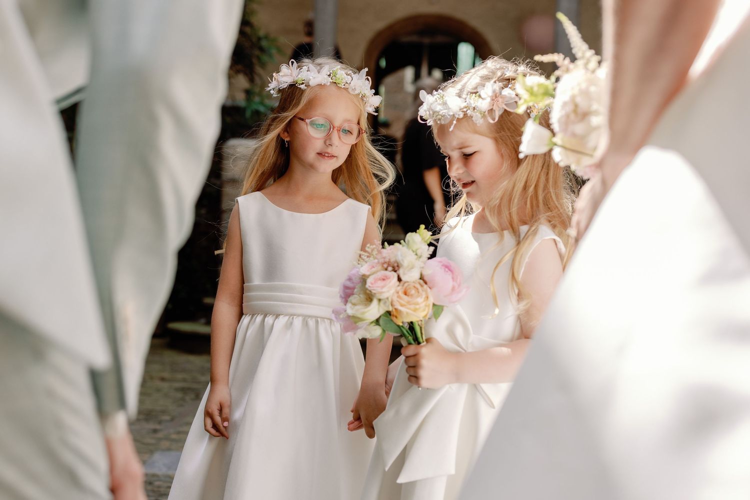 Flower girls in white dresses walk together during an elegant wedding ceremony.