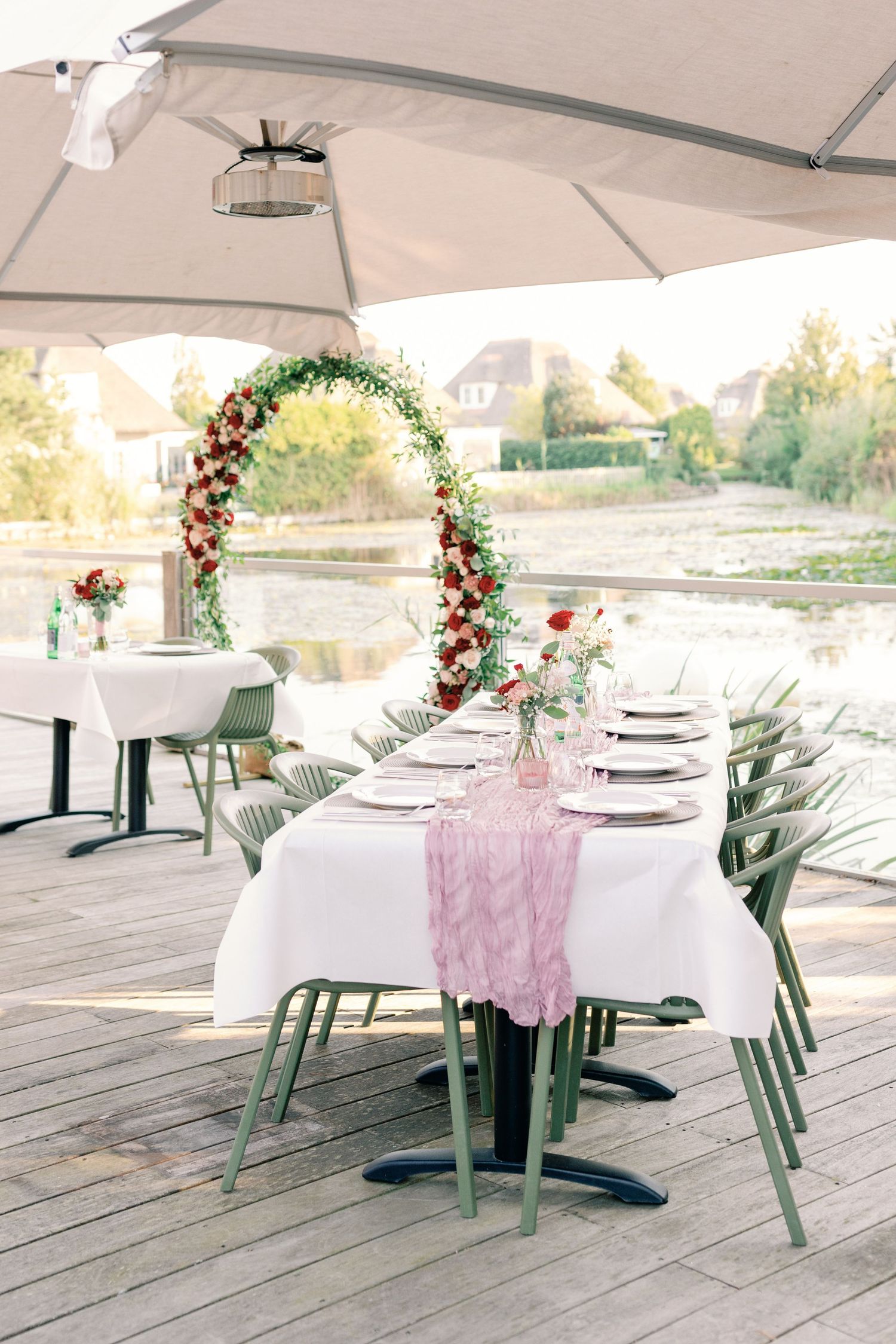 Wedding reception tables set with white linens and sage green chairs on wooden deck.