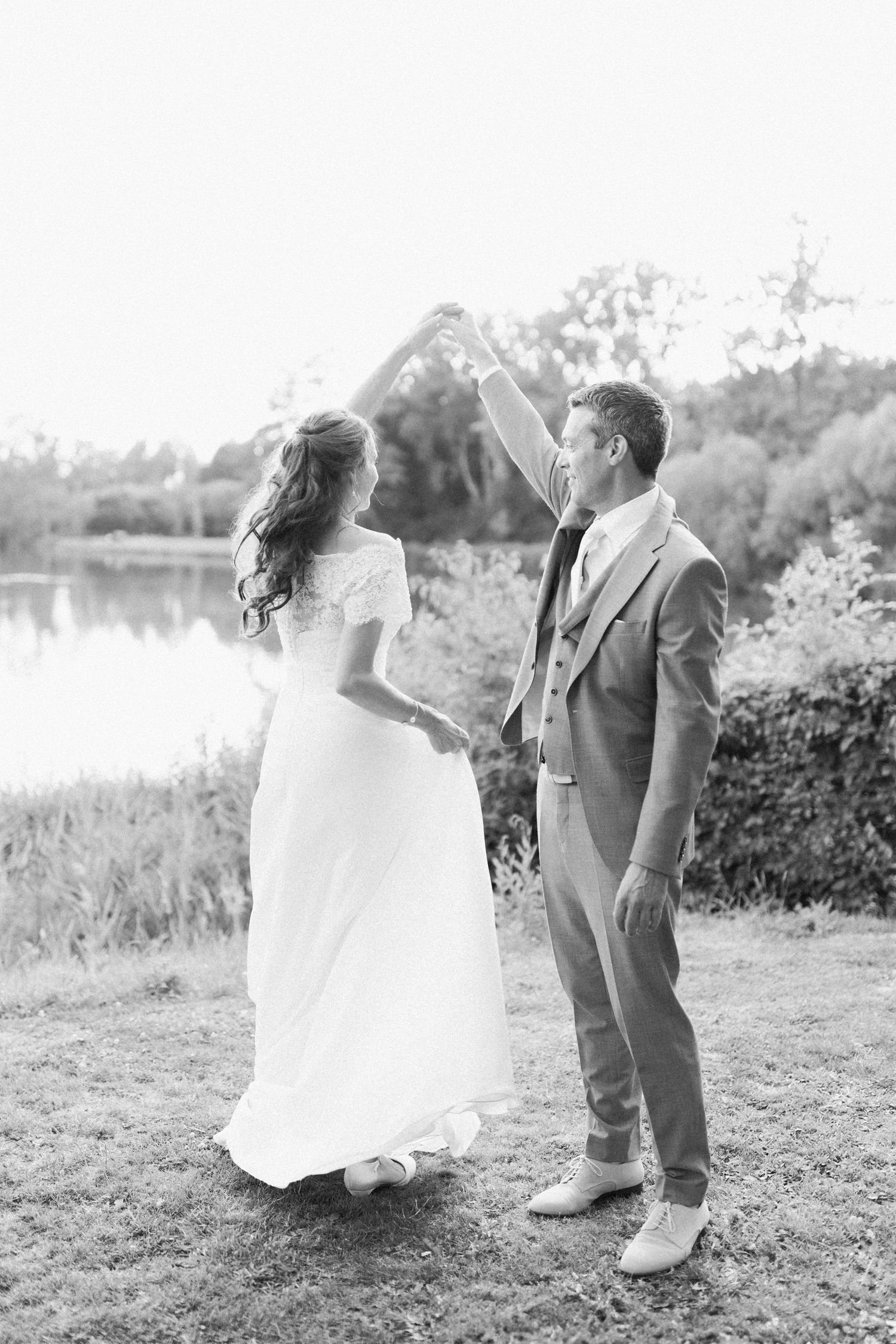 A romantic black and white wedding photo series showing a couple dancing together in an outdoor setting by a lake.