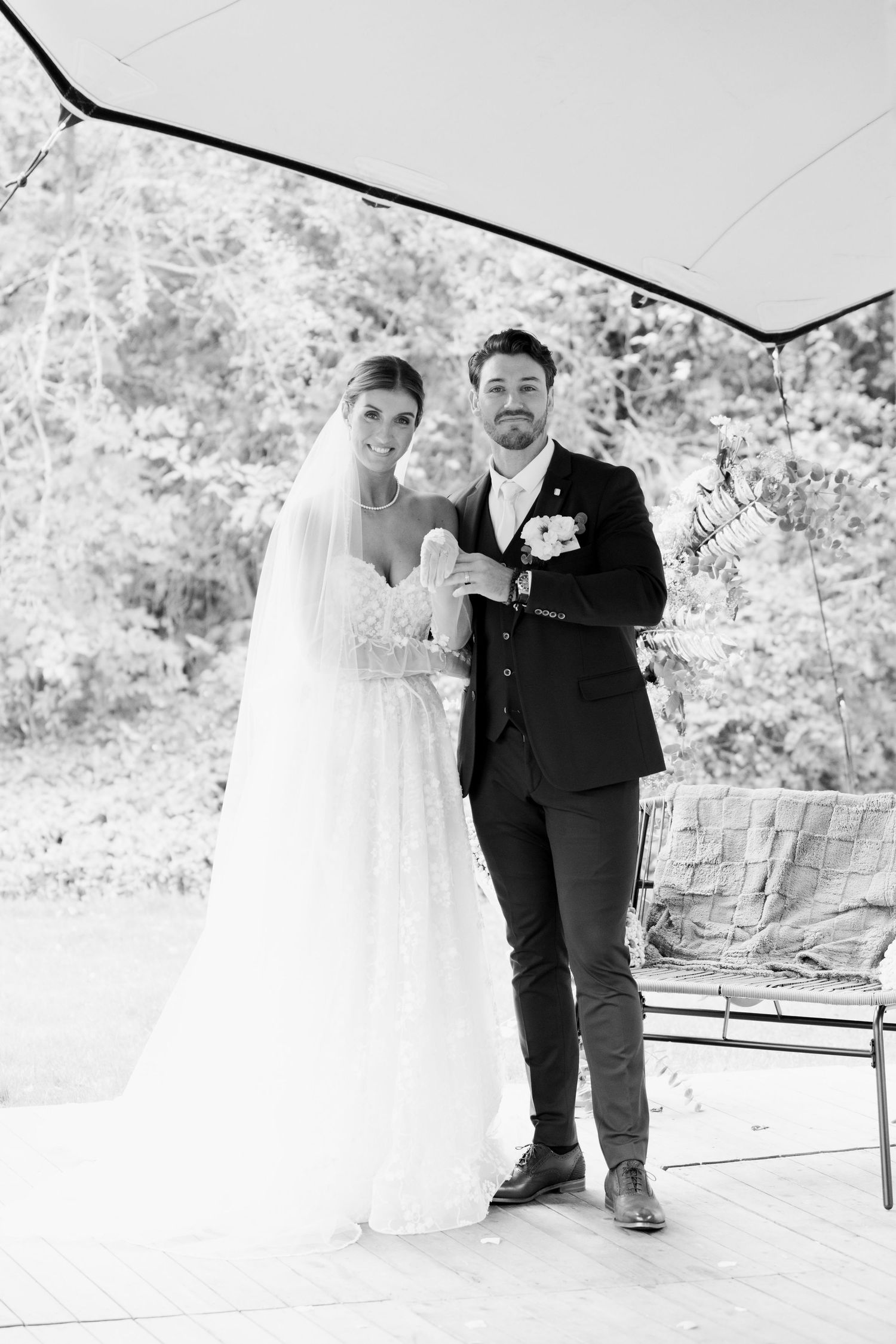A black and white wedding photo series showing a couple sitting and standing together on a bench in an outdoor setting.