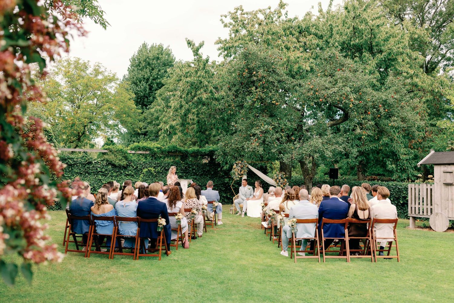 Elegant outdoor wedding reception setup with wooden chairs and tables arranged on a lush green lawn.