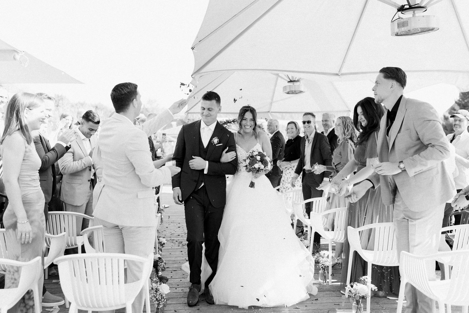 Wedding guests gather under a white tent during an outdoor celebration.