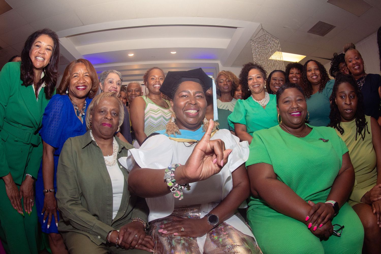 A group of people wearing green shirts and white attire gather together smiling for a celebratory photo.