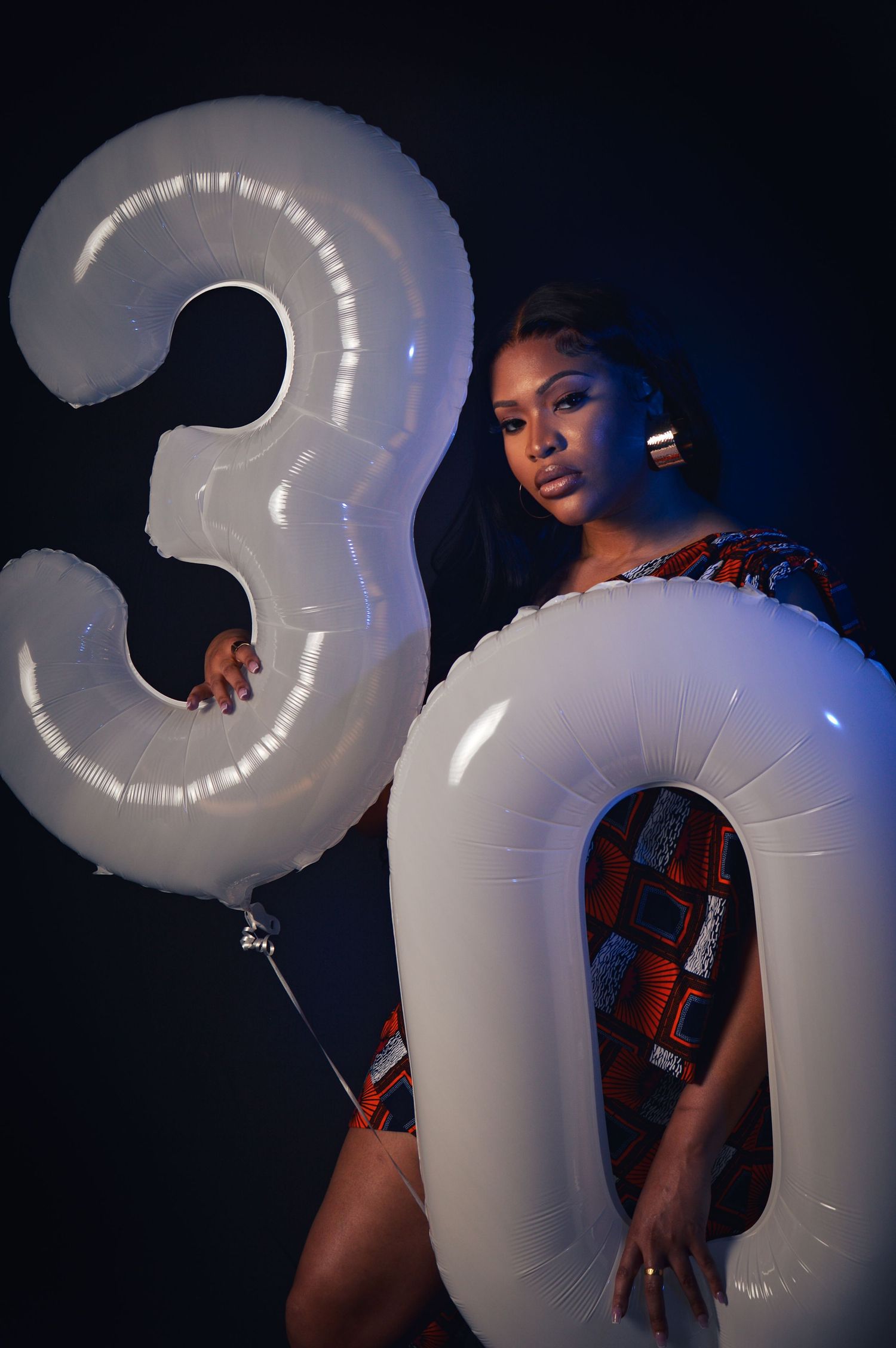 A person poses with large white inflatable number balloons forming '30' against a dark background.