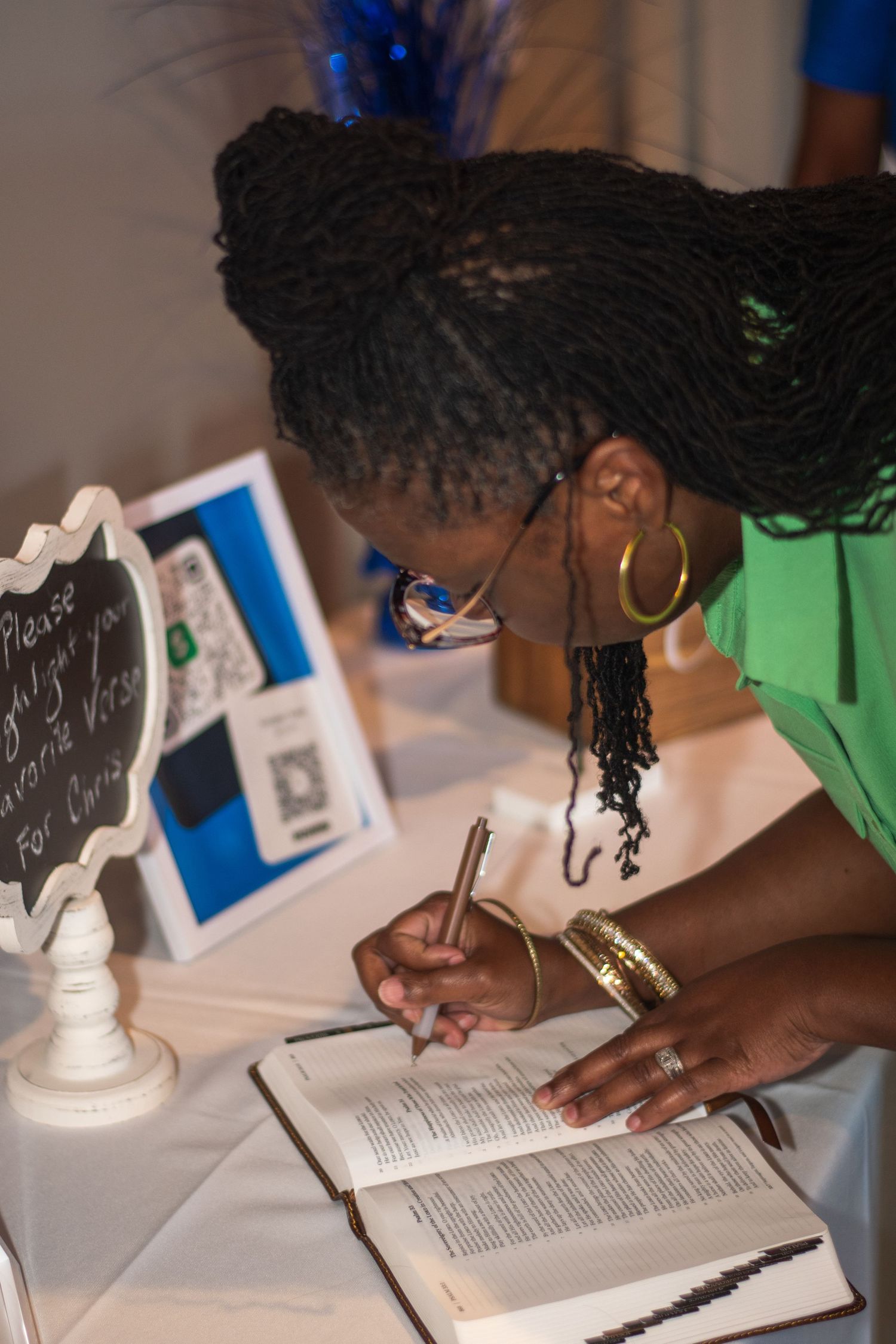 Student writing in a textbook while studying at a desk with white chess pieces visible in the background.