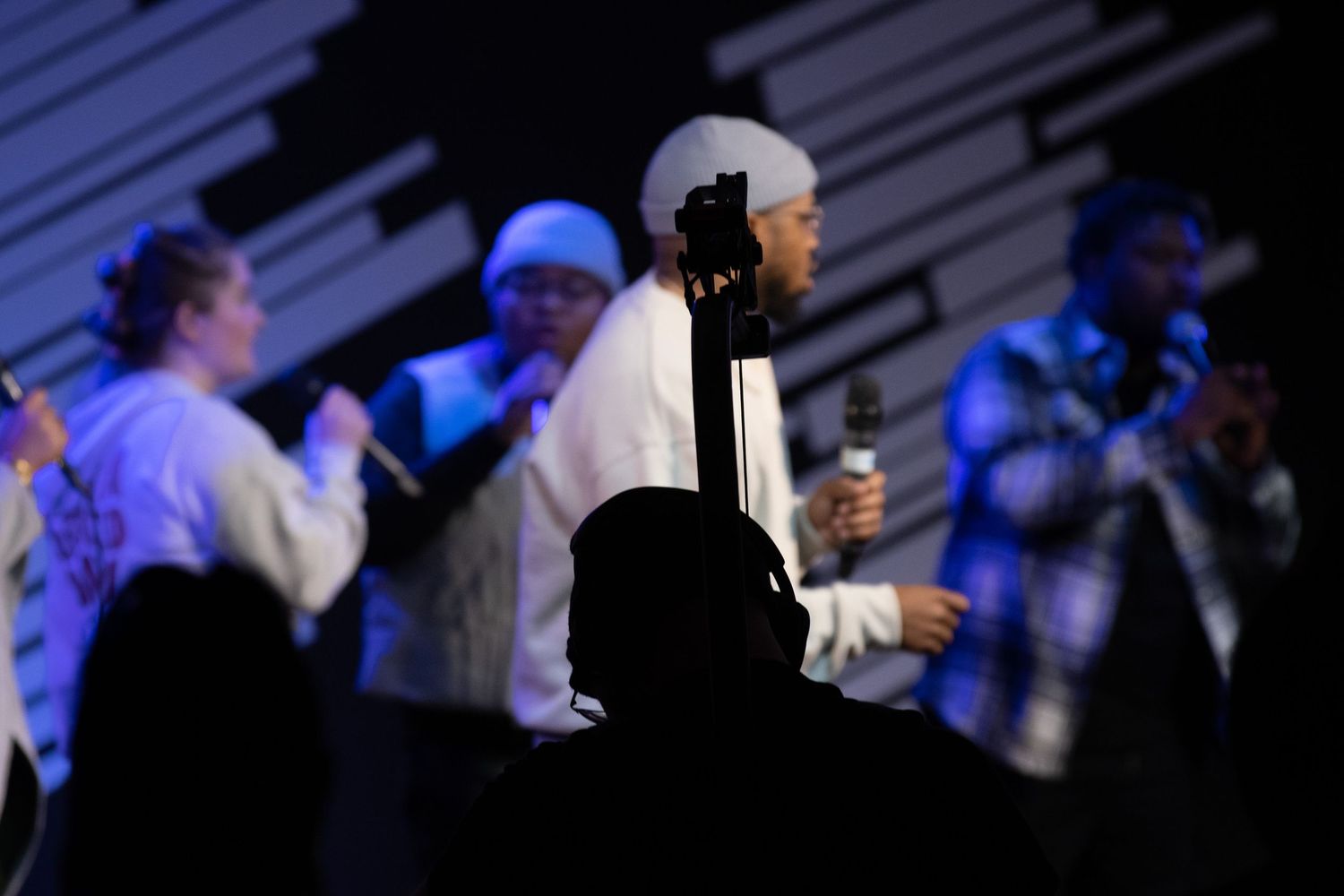 Musicians perform on a dimly lit stage with silhouettes visible against blue lighting during a concert performance.