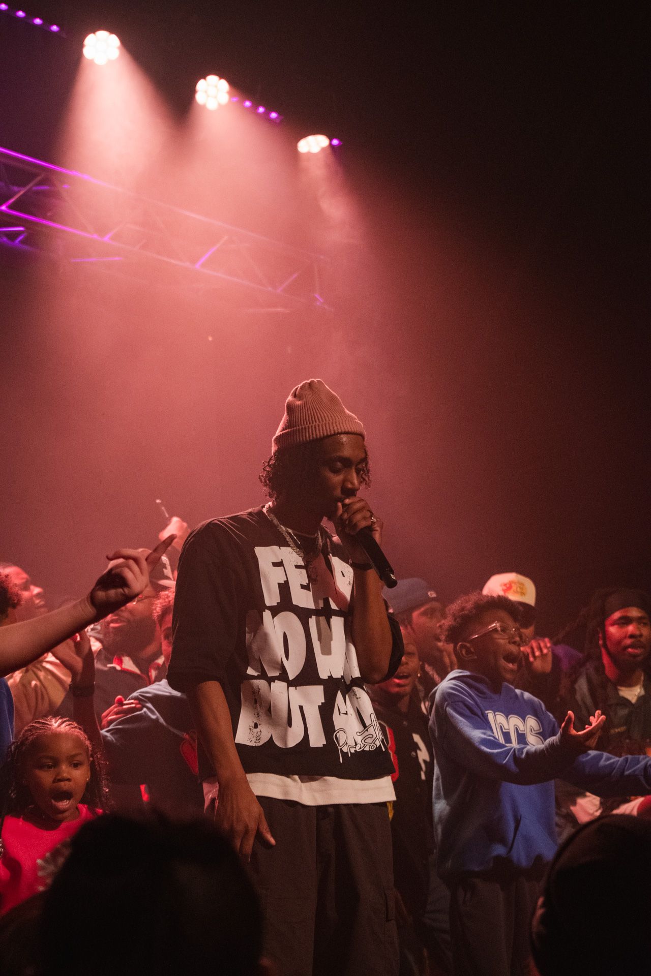 Torey D'Shaun in black and white t-shirt on stage with crowd under dramatic red lighting at live music show.