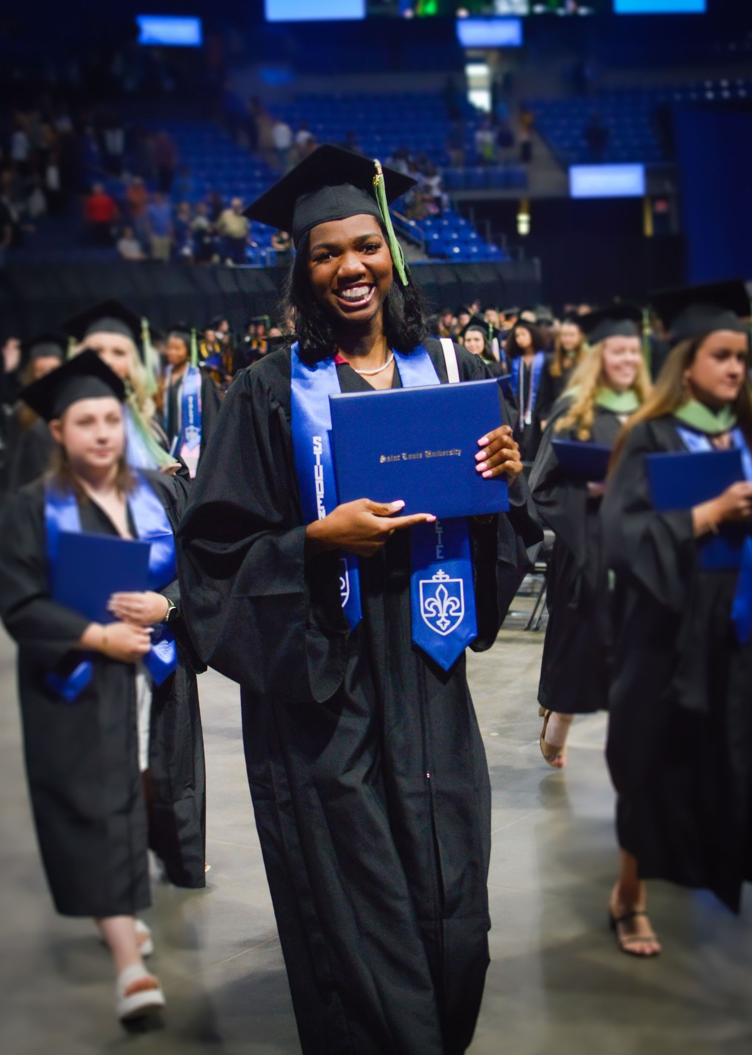Graduate celebrating with diploma during commencement ceremony in arena.