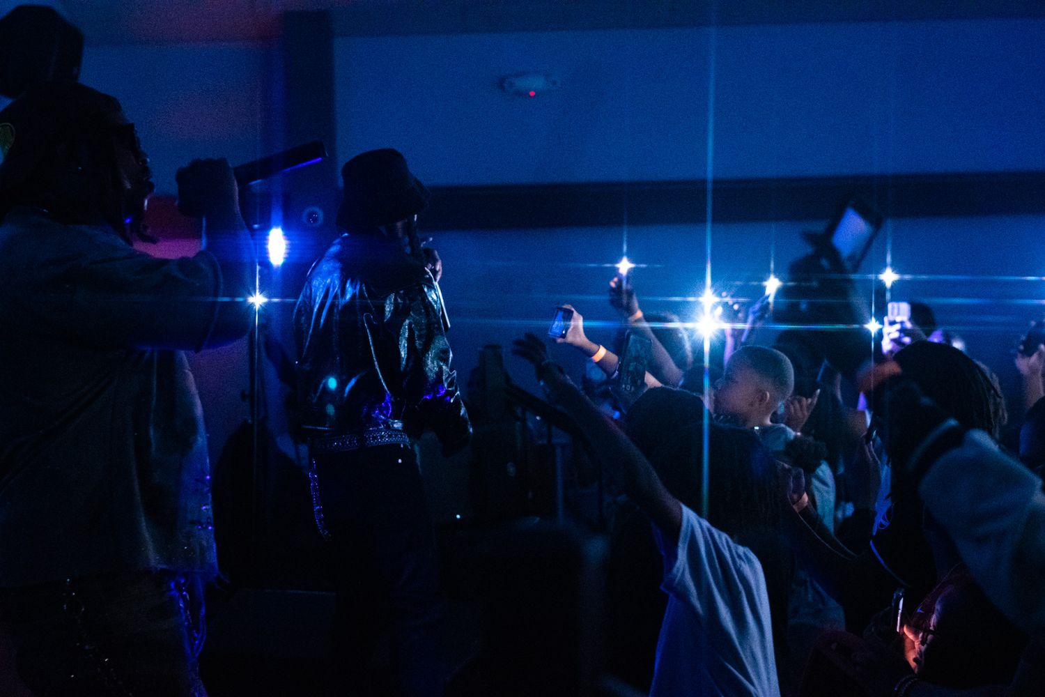 Concert crowd silhouettes against dark blue stage lighting during a nighttime performance.