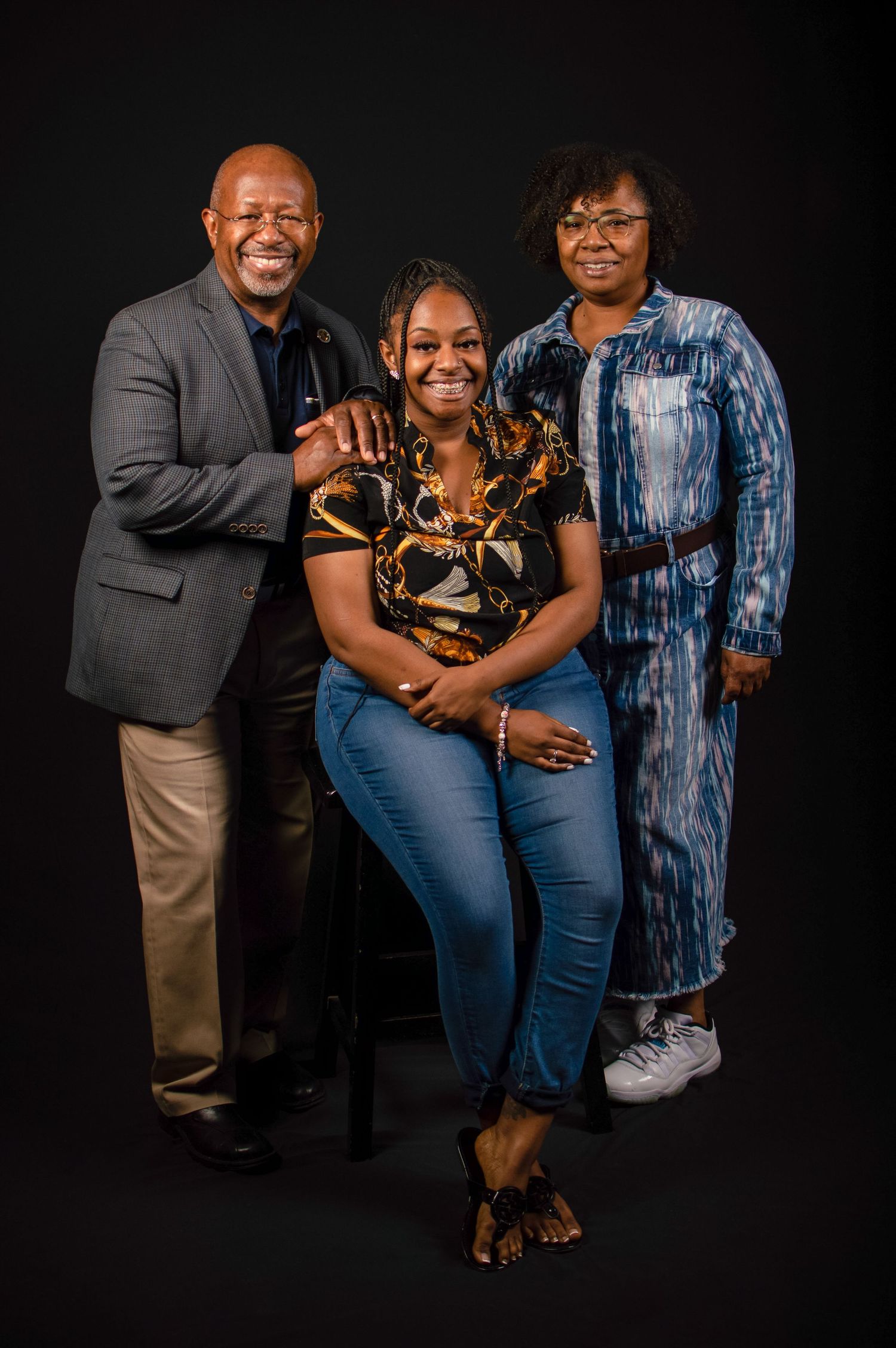 A family portrait against a black background showing three people dressed in business casual attire posing together.