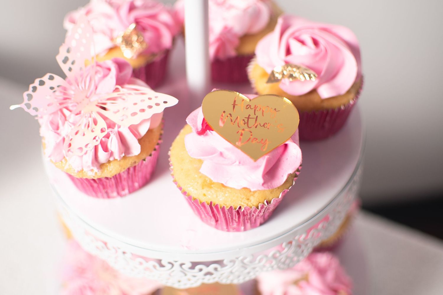 Pink frosted cupcakes with delicate butterfly decorations displayed on elegant white cake stands.