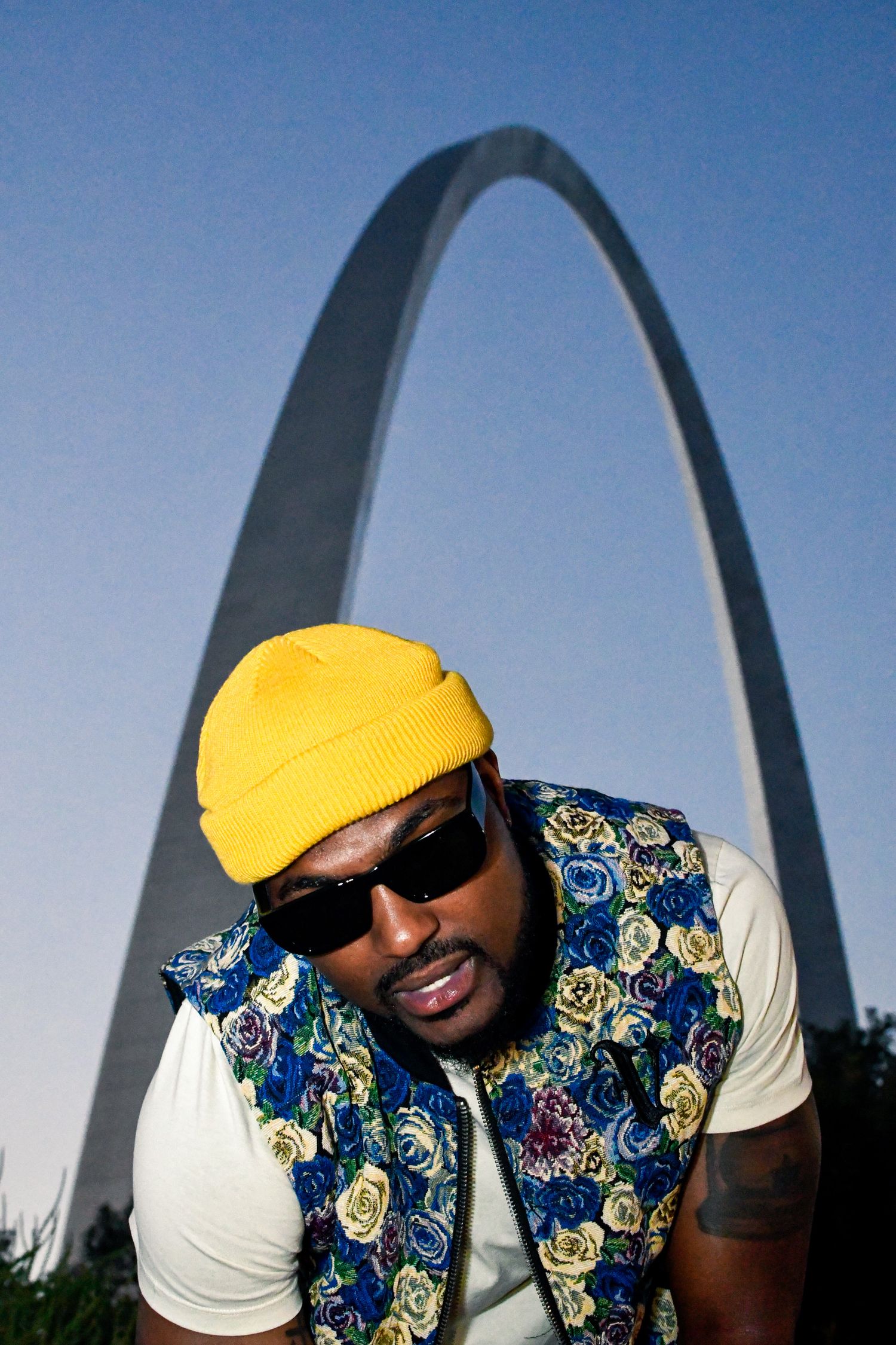 Person wearing yellow beanie and floral vest poses in front of the Gateway Arch in St. Louis, Missouri.