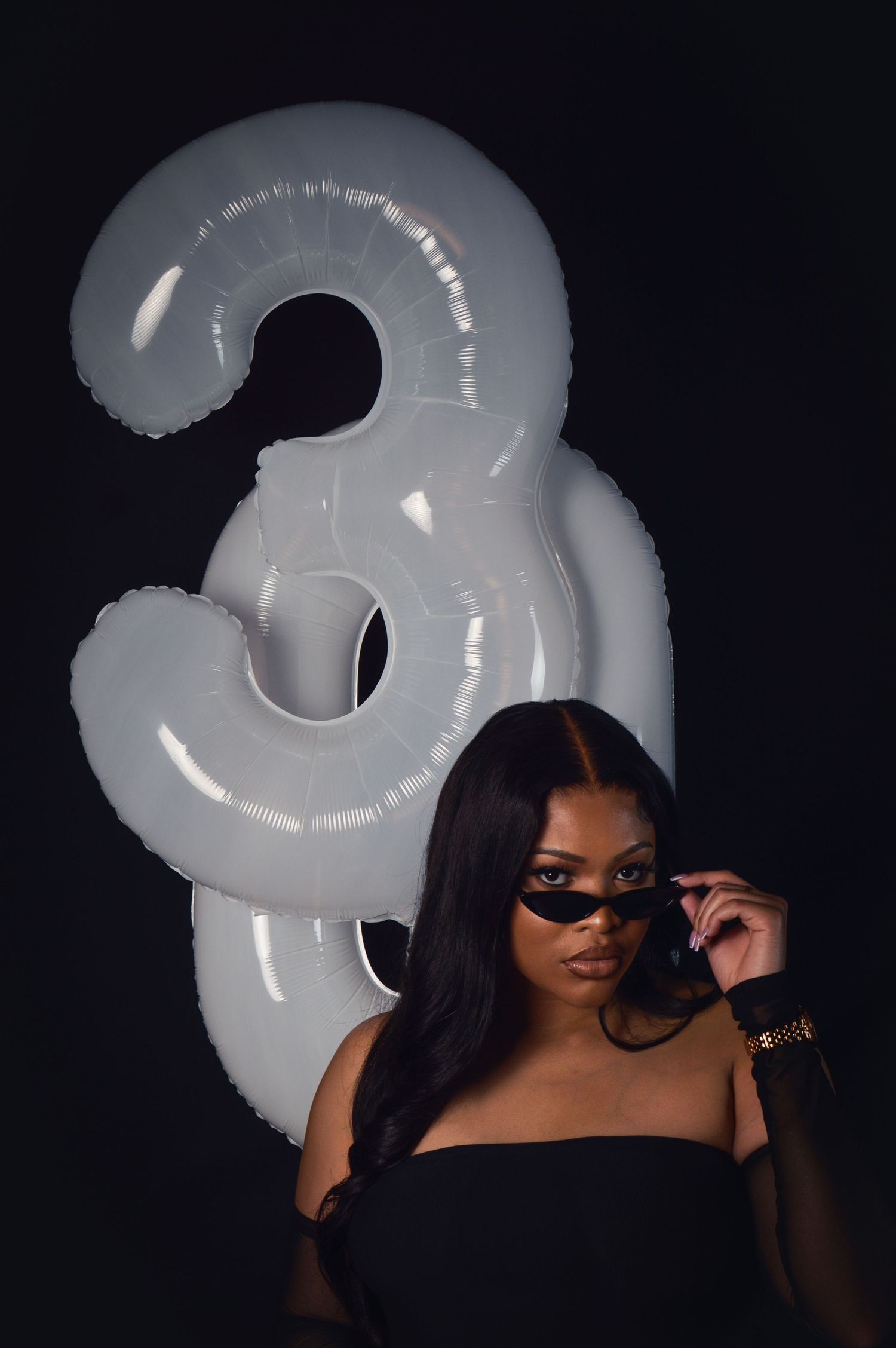 A person poses with a white balloon number 3 against a dark background in a stylized photoshoot series.