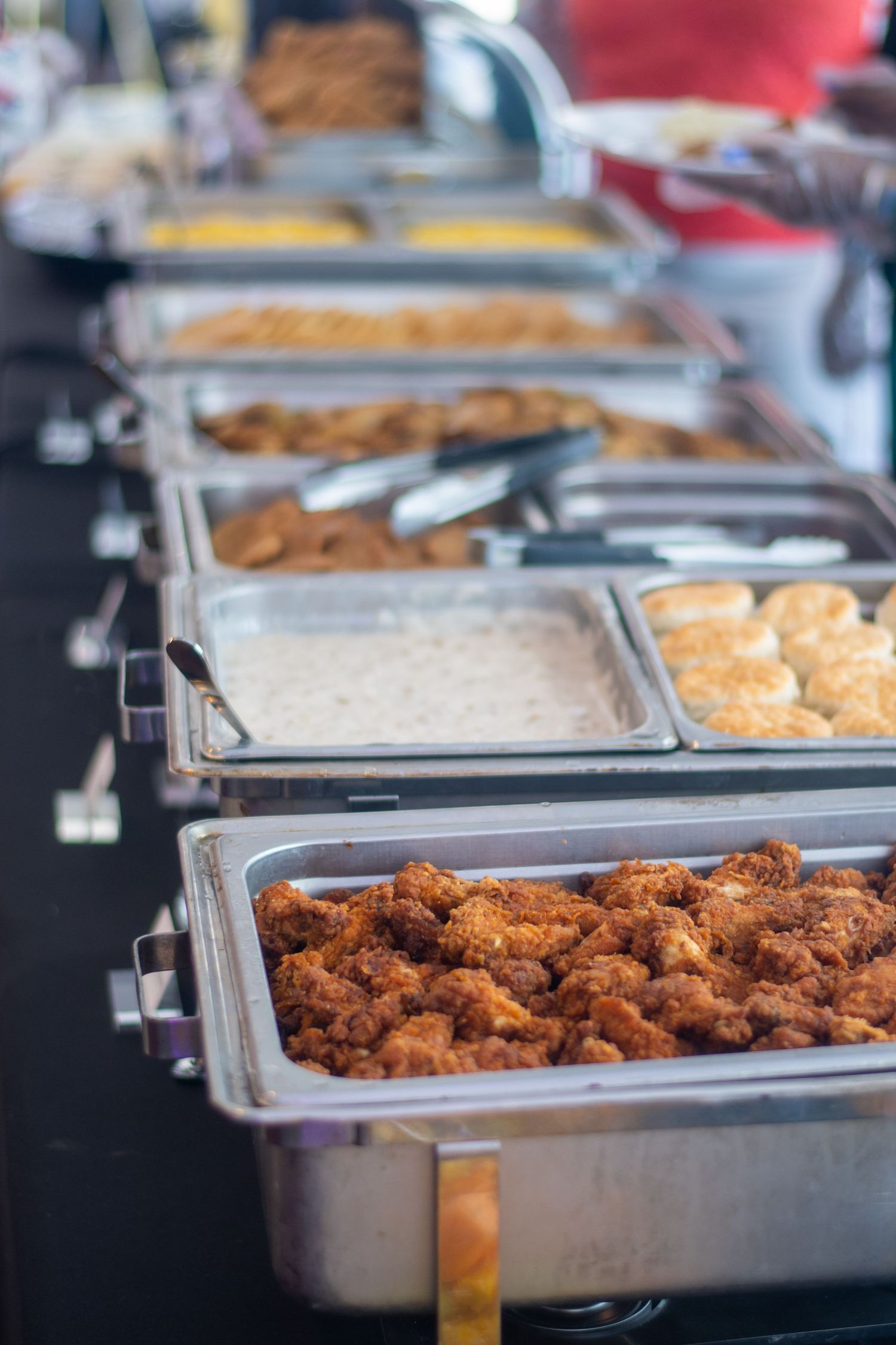 Buffet line of stainless steel catering trays filled with fried foods and side dishes.