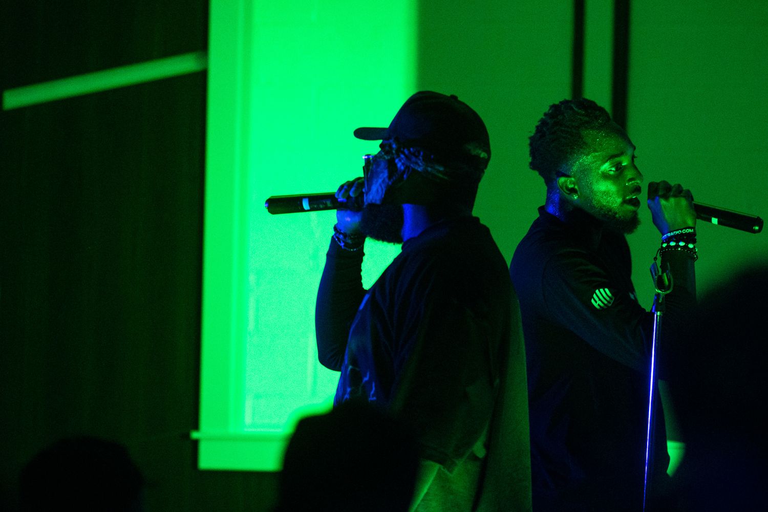Silhouettes of concert performers on stage illuminated by bright green lighting effects.