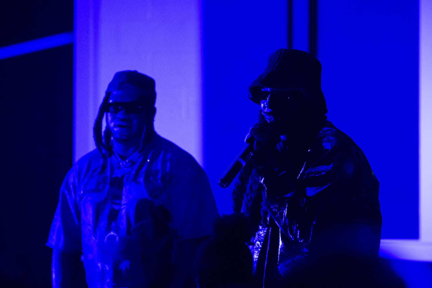 Two silhouettes perform on stage in dramatic blue lighting creating a moody atmospheric effect.
