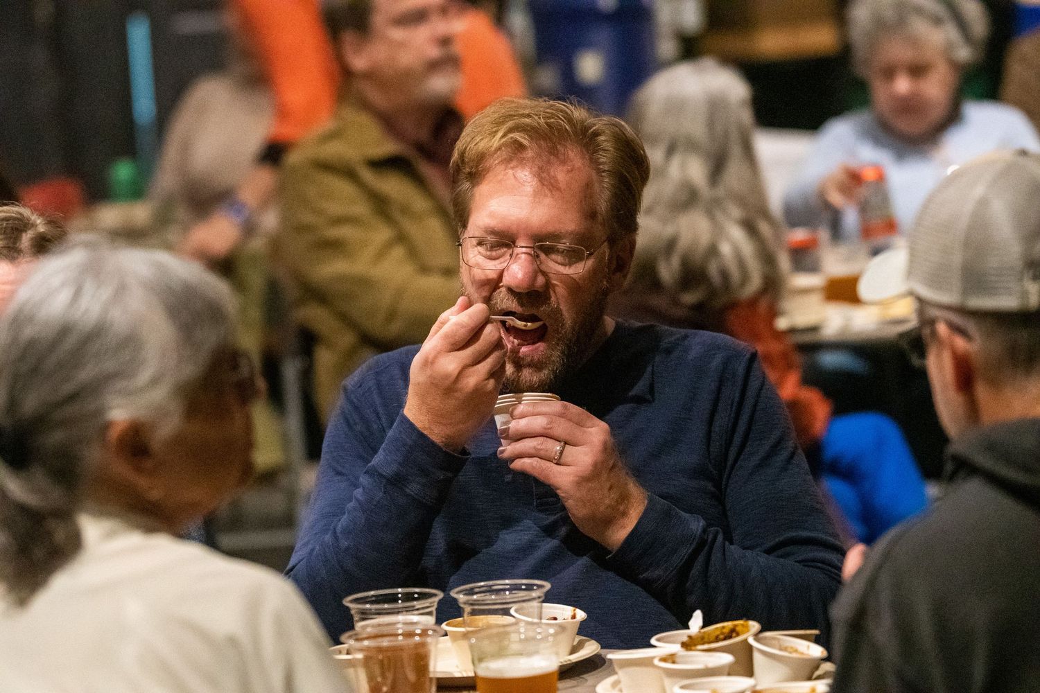 People gather at a social event enjoying food and drinks in a casual indoor setting.