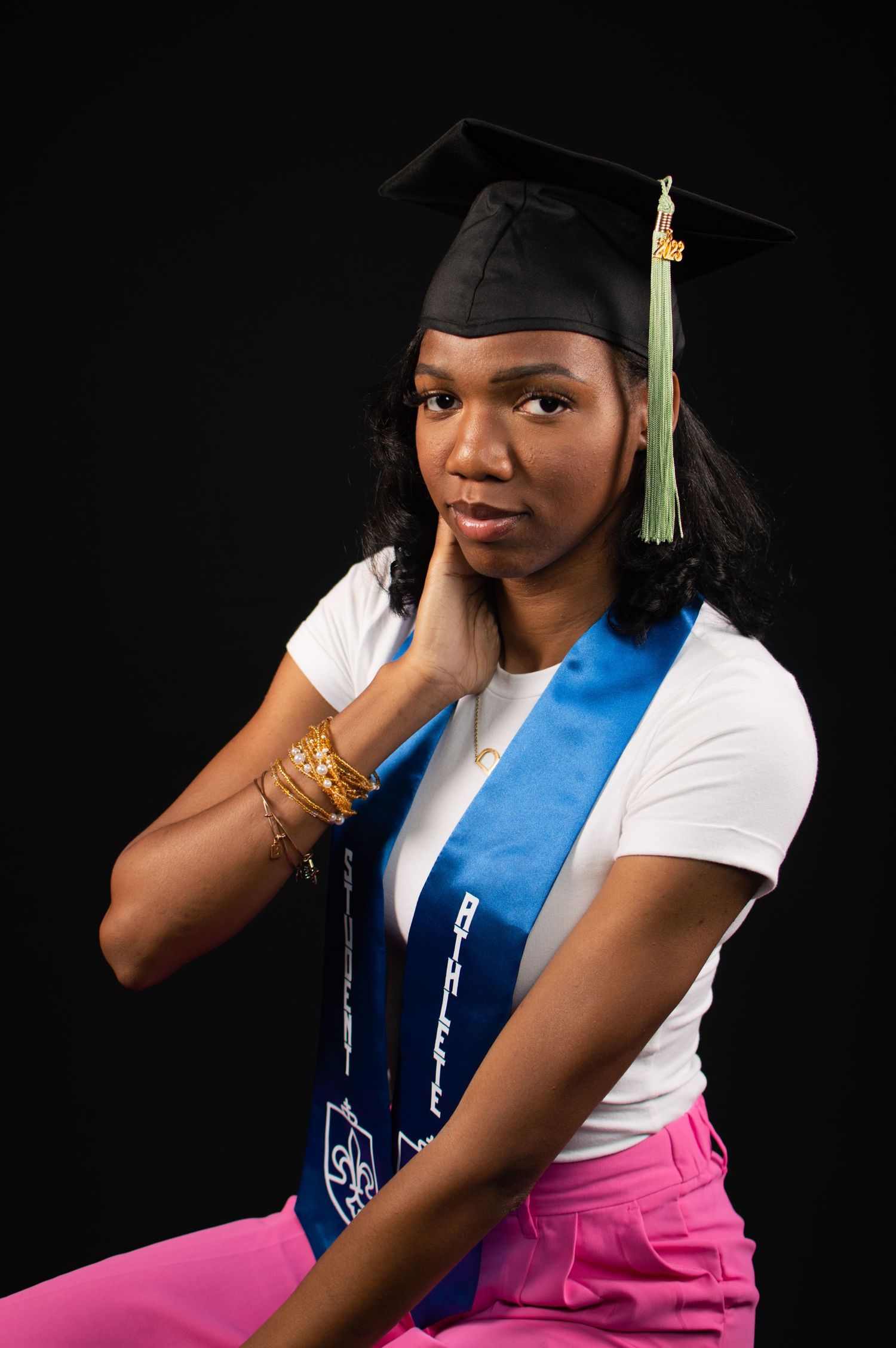 Graduate in casual attire and blue stole poses thoughtfully during photo session.