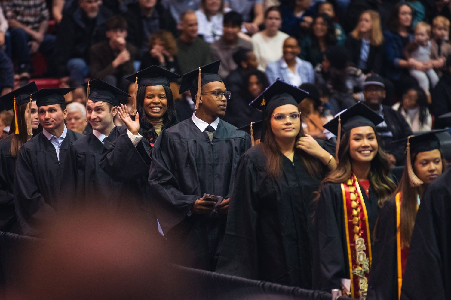 Graduates in black caps and gowns stand together during a university commencement ceremony.