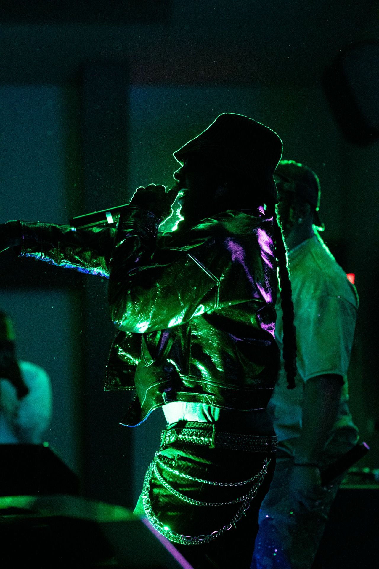 A sequence of dark photos showing a figure illuminated by green and purple stage lighting during a performance.