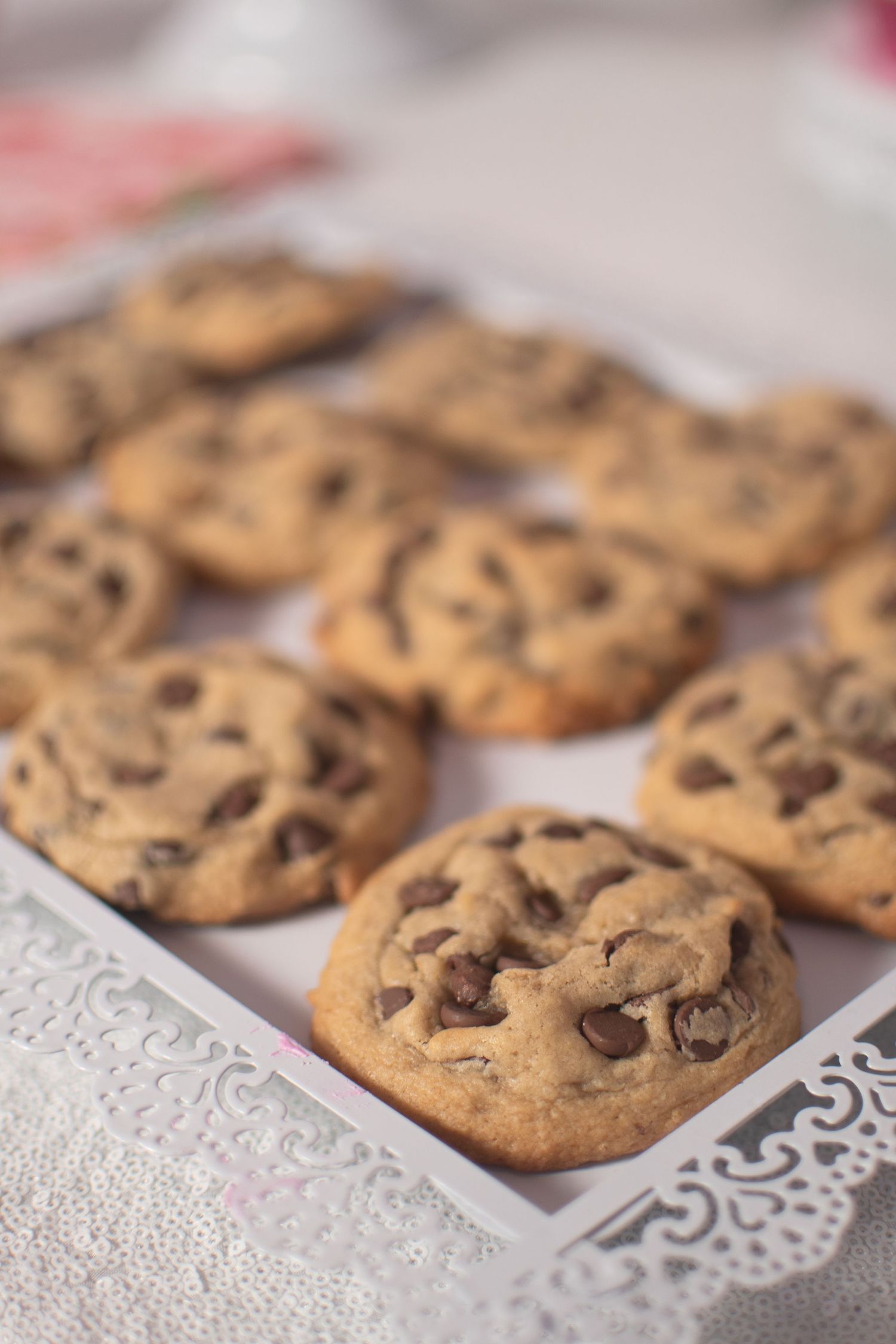 Freshly baked chocolate chip cookies arranged in rows on a decorative white paper doily.