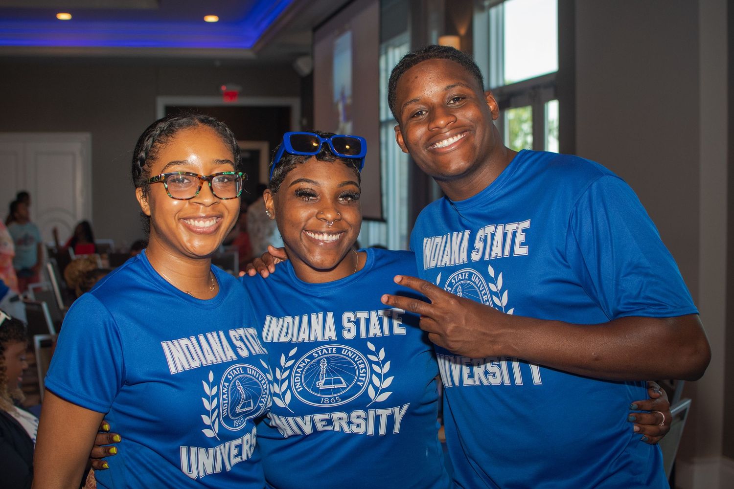 A group of people wearing blue Indiana State University shirts gather together at an event.