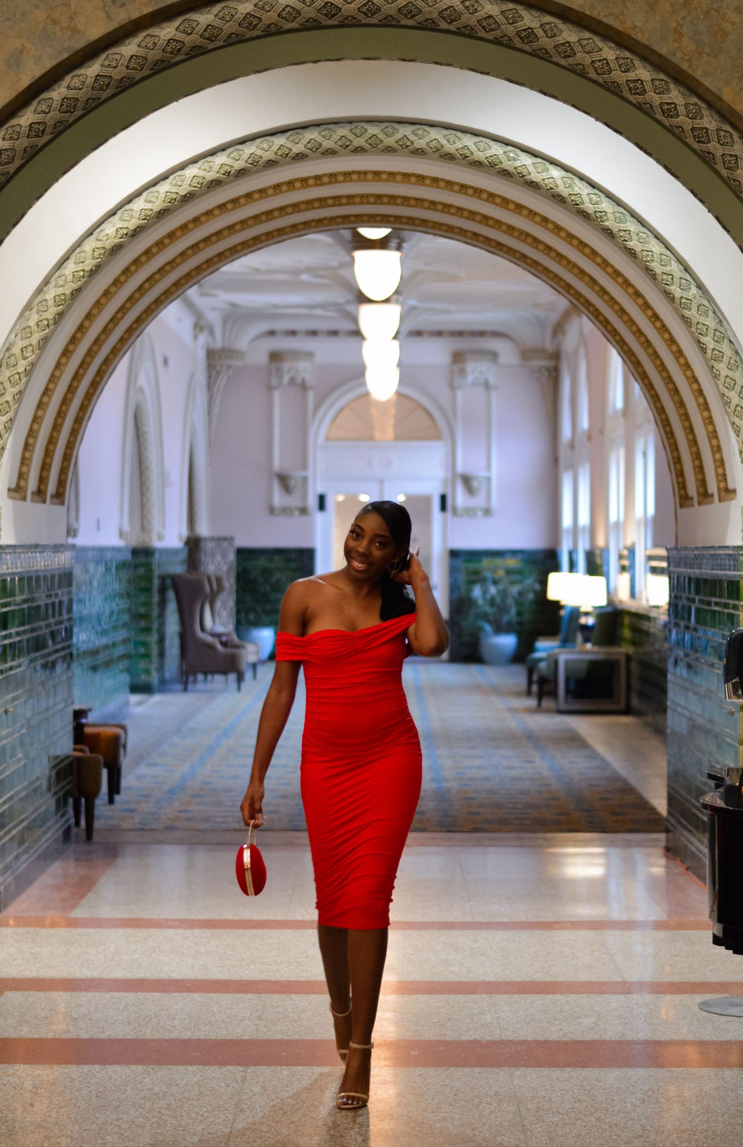 A person in a red dress walks through an ornate arched hallway with decorative tile walls and marble floors.