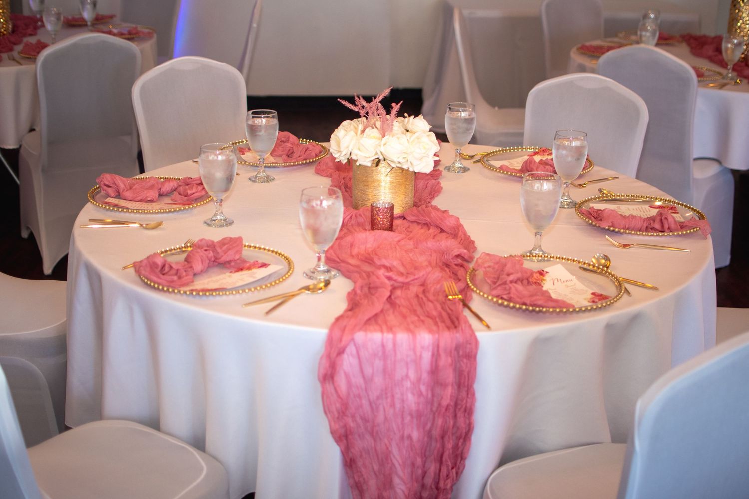 Elegant table settings with white linens and pink decorative elements at a formal event.