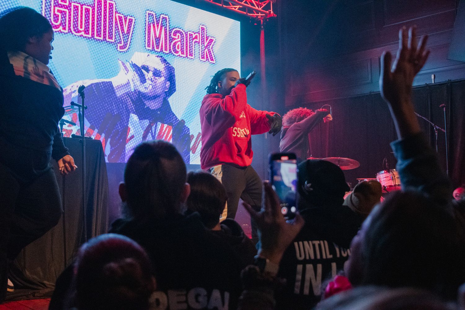 Concert performers on stage with dramatic pink and blue lighting effects during a live music performance.