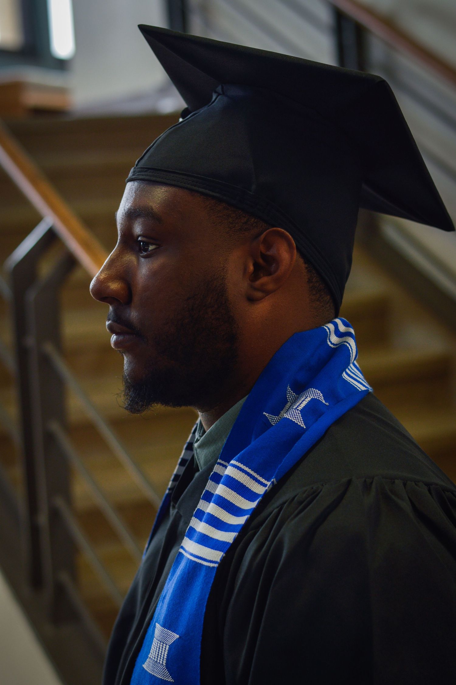 Graduate in black cap and gown with blue stole photographed in profile.