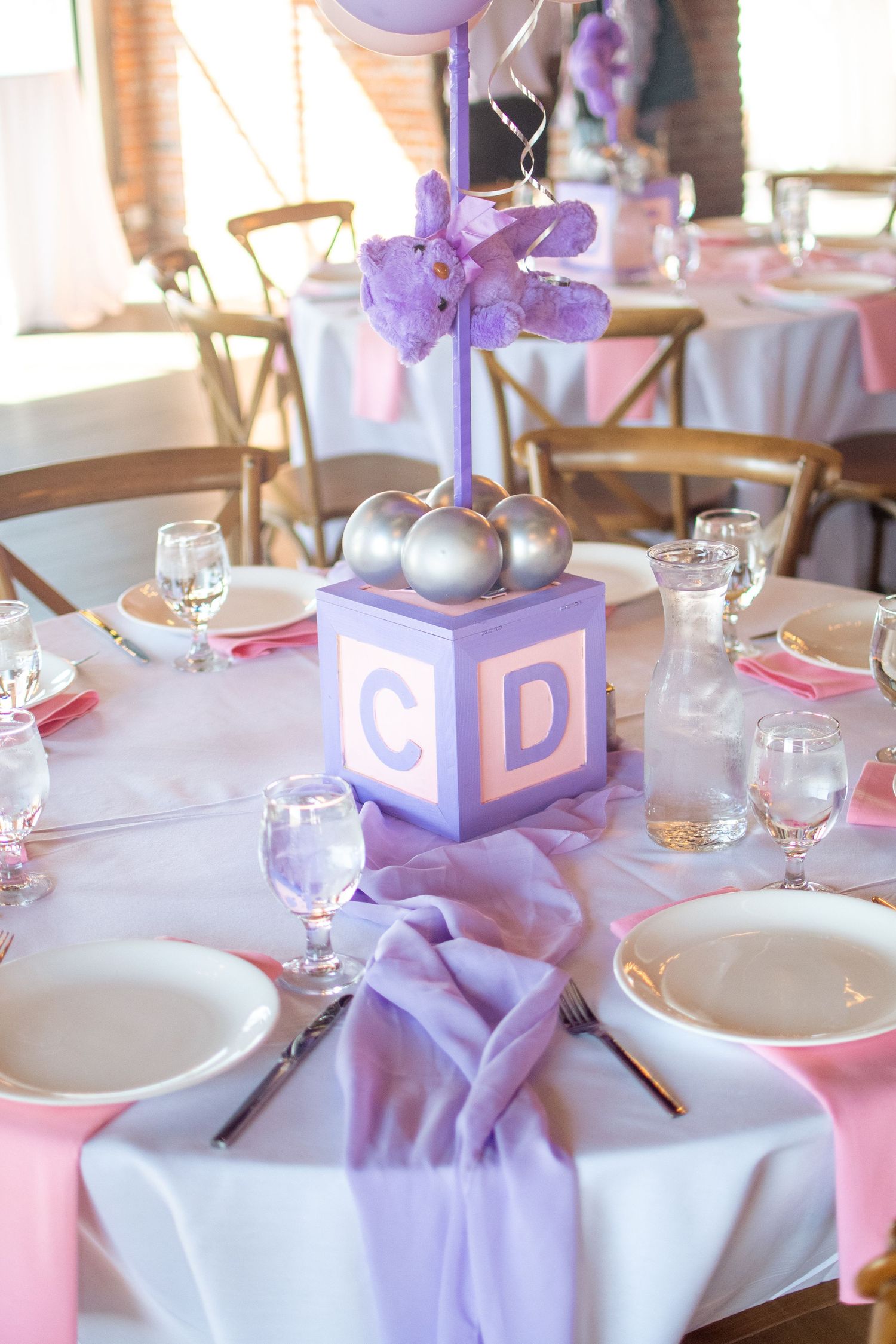 Elegant table setting with purple and pink decor featuring baby blocks and floral centerpieces.