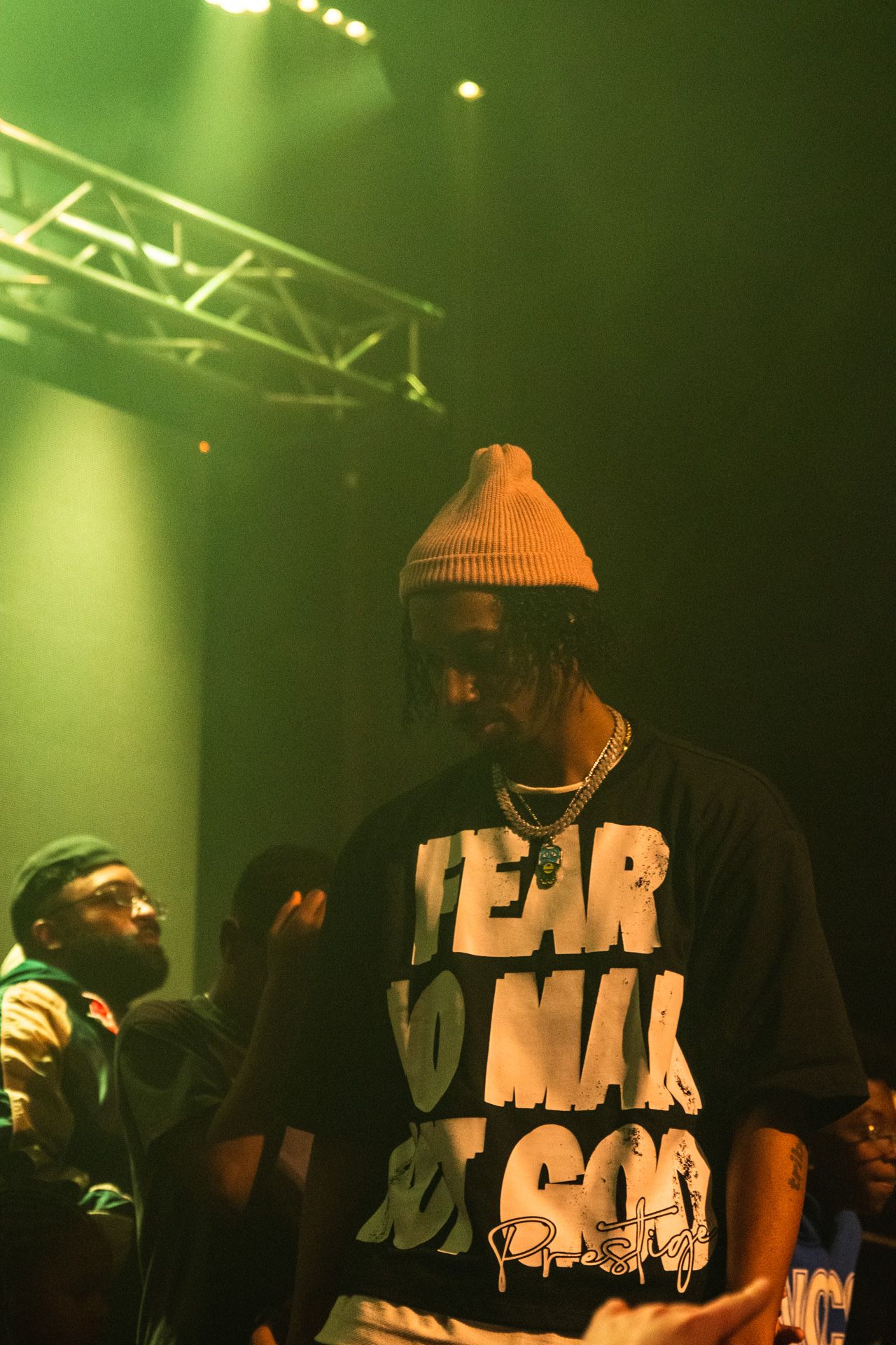 Hip hop performers on stage bathed in green lighting during a nighttime concert performance.